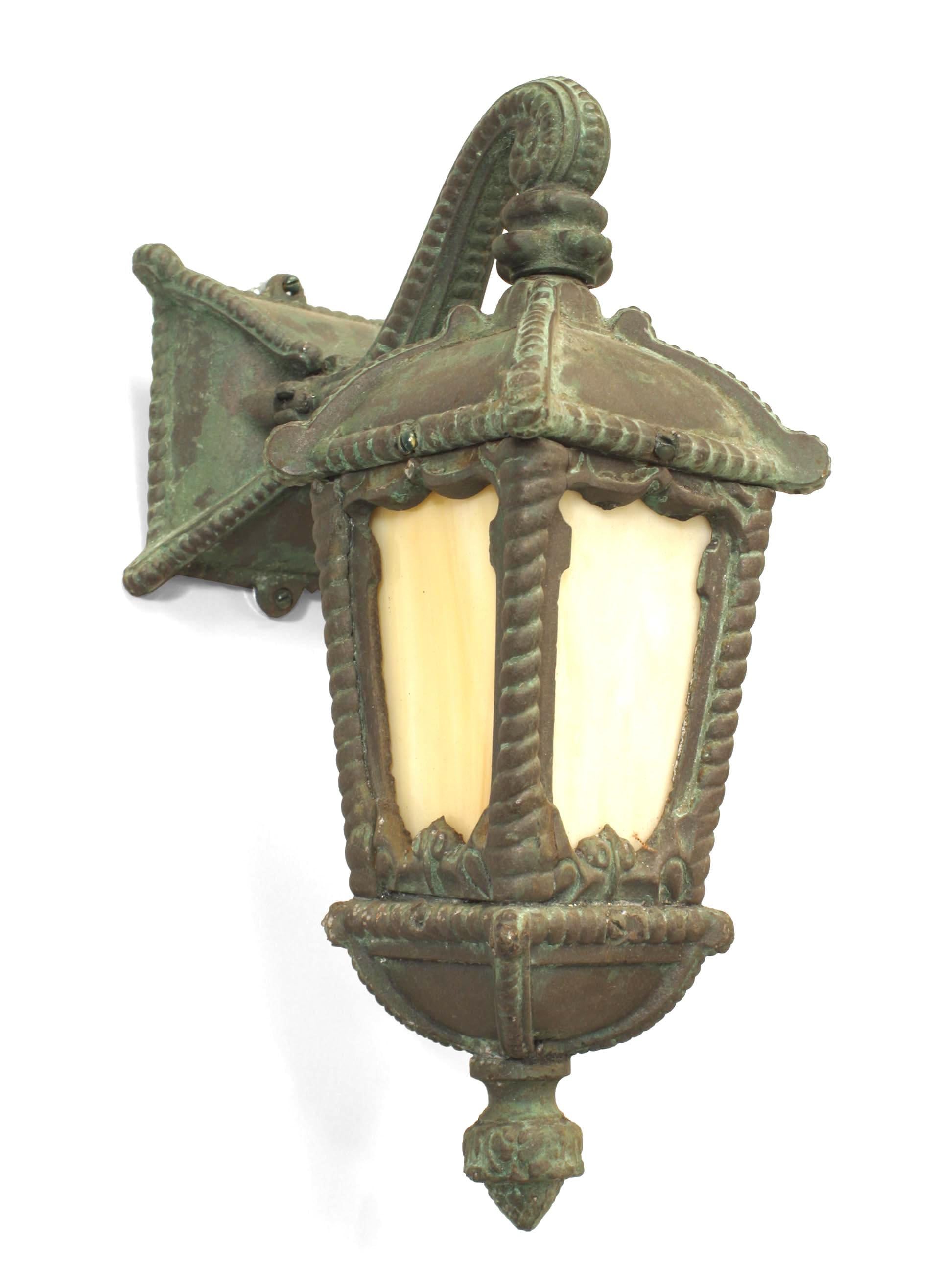 Pair of American Victorian green patinated iron outdoor wall sconces with rope trim and a scroll arm supporting a square lantern with four stained glass panels. (PRICED AS Pair) Two pairs are avaliable. One pair has different glass insets in a