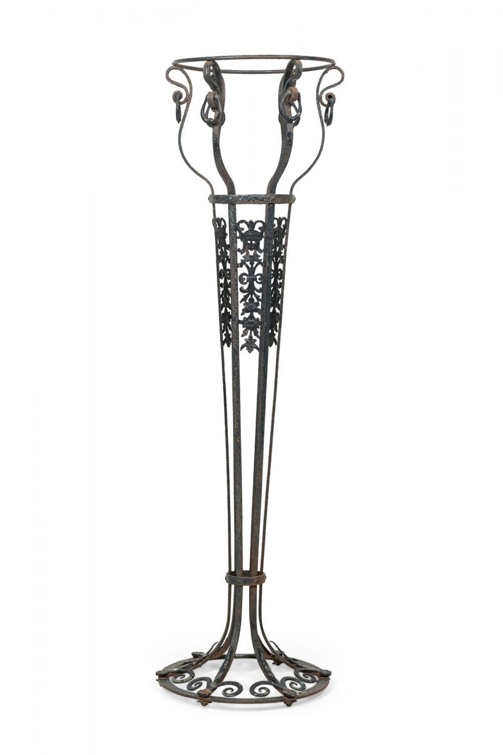 PAR de jardineras de hierro forjado con un diseño perforado con una fila superior de pestillos decorativos concéntricos colgantes, 3 columnas con volutas y follaje, que se estrechan hacia un pie circular con volutas. (PRECIO POR PAR)

Acabado