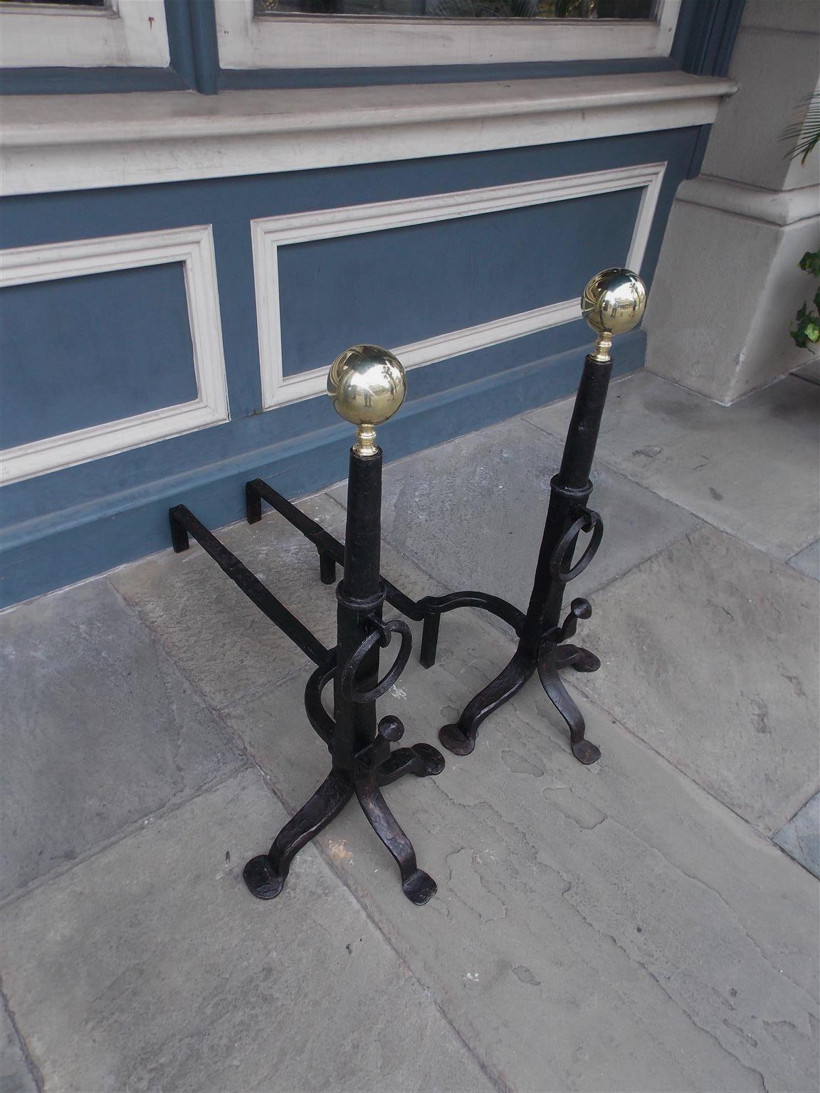 Pair of American wrought iron and brass ball top andirons with circular turned ringed columns, decorative centered rings, flanking spit hooks, curvature dog legs, and terminating on scrolled tripod penny feet, Early 19th century. Centered columns