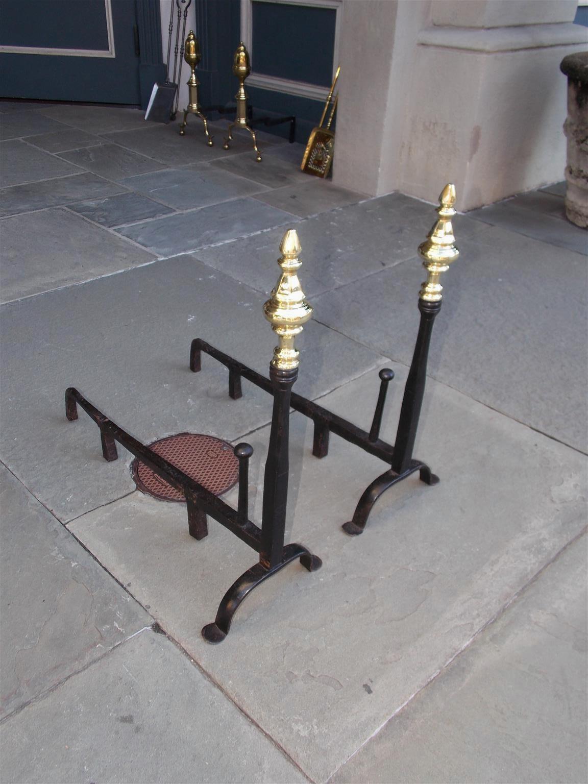 Pair of American wrought iron and brass faceted finial andirons with tapered columns, squared plinths, matching log stops, original dog legs, and resting on penny feet, Late 18th century.