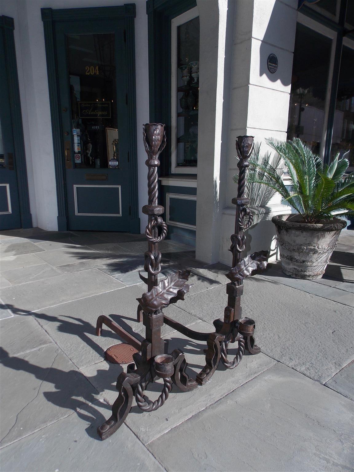 Pair of American wrought iron and faux painted bronze andirons with flanking foliage  finials, spiral and ringed centered columns, squared foliage plinths, matching rear dog legs, and terminating on shaped scrolled knees with decorative spiral rings