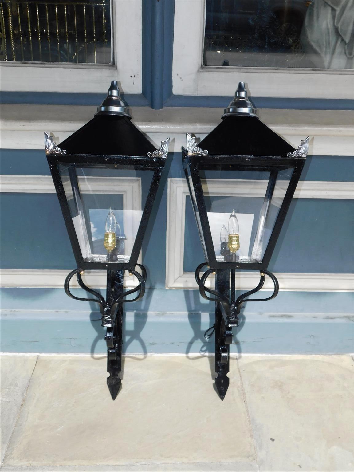 Pair of American wrought iron, paneled glass, and spelter finial decorative wall lanterns mounted on the original scrolled iron brackets. Originally gas and have been electrified with single interior socket. Mid 19th century.