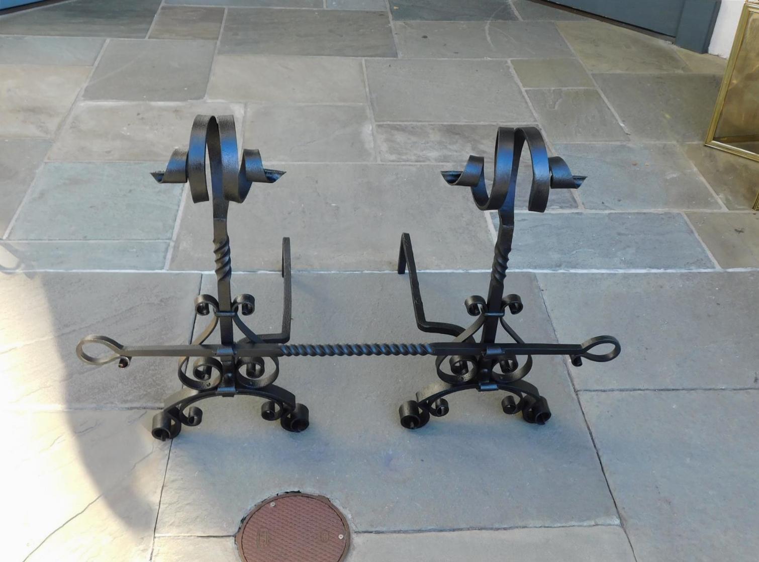 Pair of American wrought iron flanking scrolled finial andirons with centered spiraled columns, scrolled plinths, decorative spiraled scrolled cross bar, and resting on matching scrolled legs. Mid-19th century.