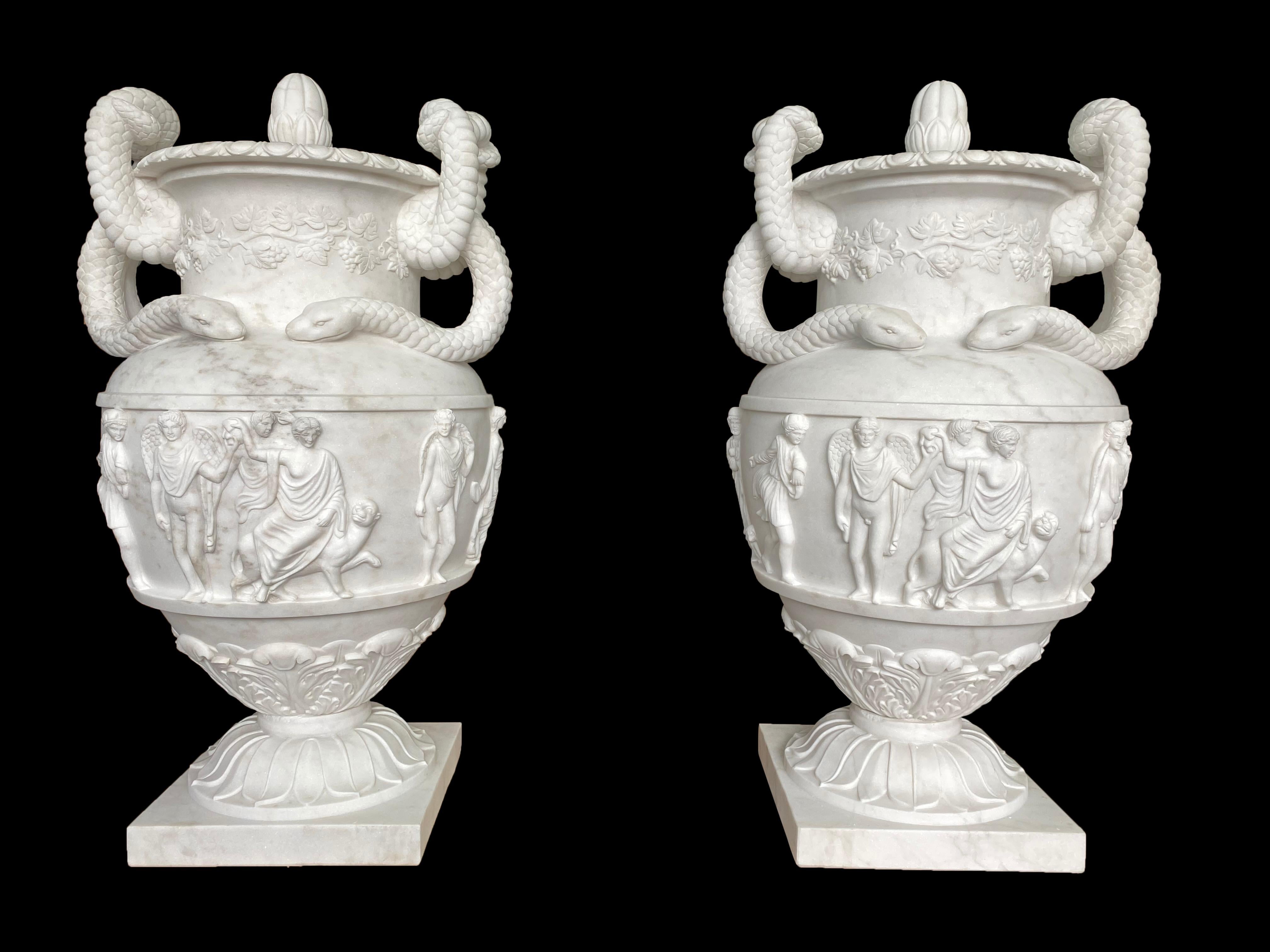 A monumental pair of regency style white Carrara marble urns, late 20th century. This magnificent pair of urns recalls the form of an Ancient Greek krater, a large vessel for mixing wine. The entire urn is dedicated to the God of Wine Bacchus