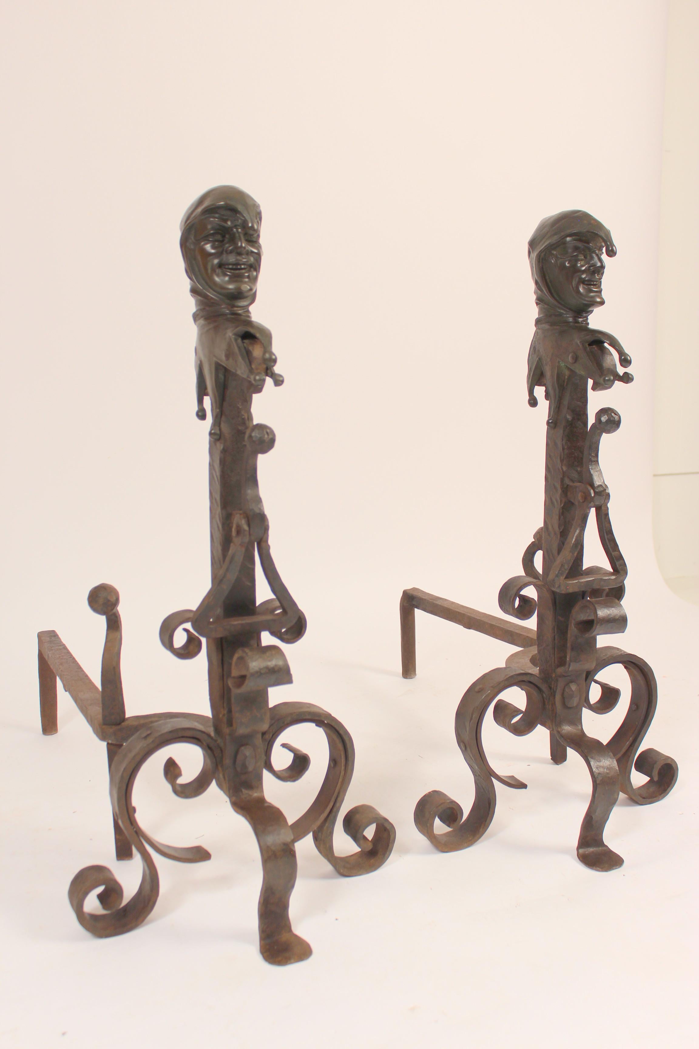 Pair of wrought iron and bronze andirons with bronze jester faces, circa 1920s. The jester faces are bronze and the rest of the andirons are wrought iron.