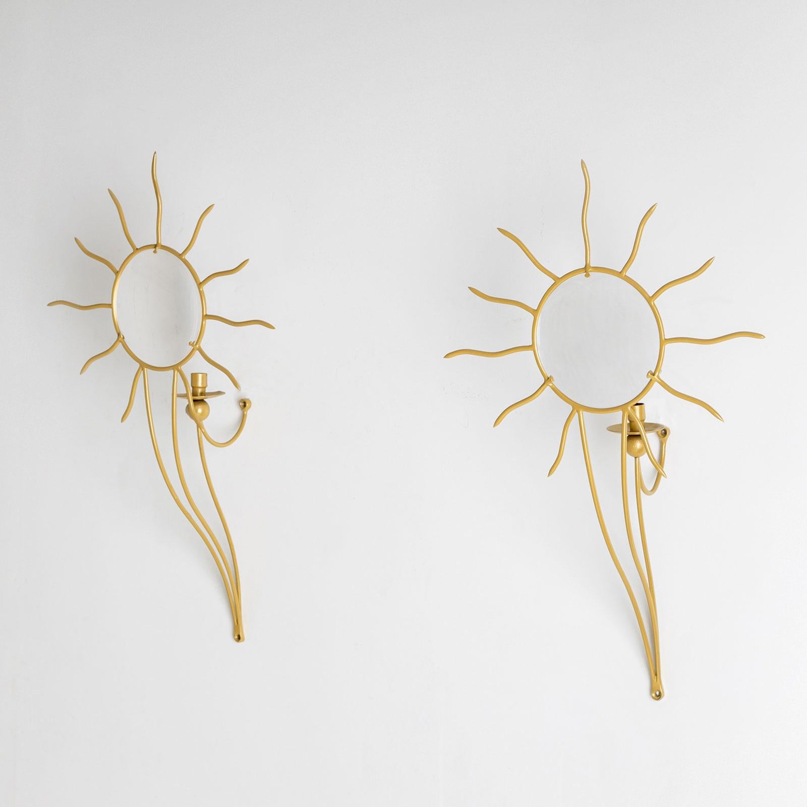 A pair of Soleil wall appliqués with space for one candle and a convex glass panel with a sun motif. The glass panel magnifies the candle behind it, enhancing the light effects. The elegant frame is gold-colored and is fixed to the wall at two