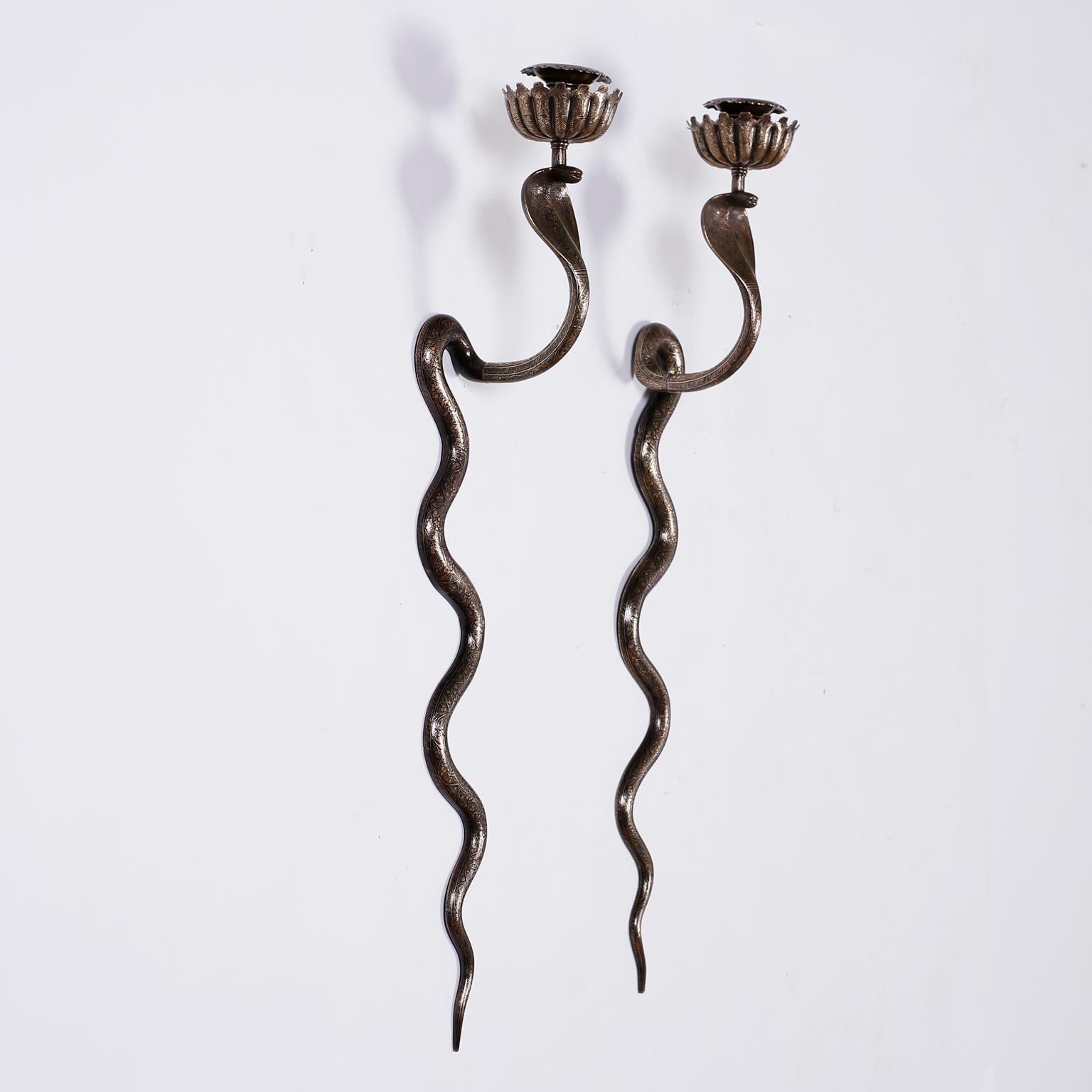 Pair of brass wall sconces in the form of cobras or snakes with floral candle cups at the top, hand hammered symbolic designs throughout, and traces of enamel over a bronze like patina.