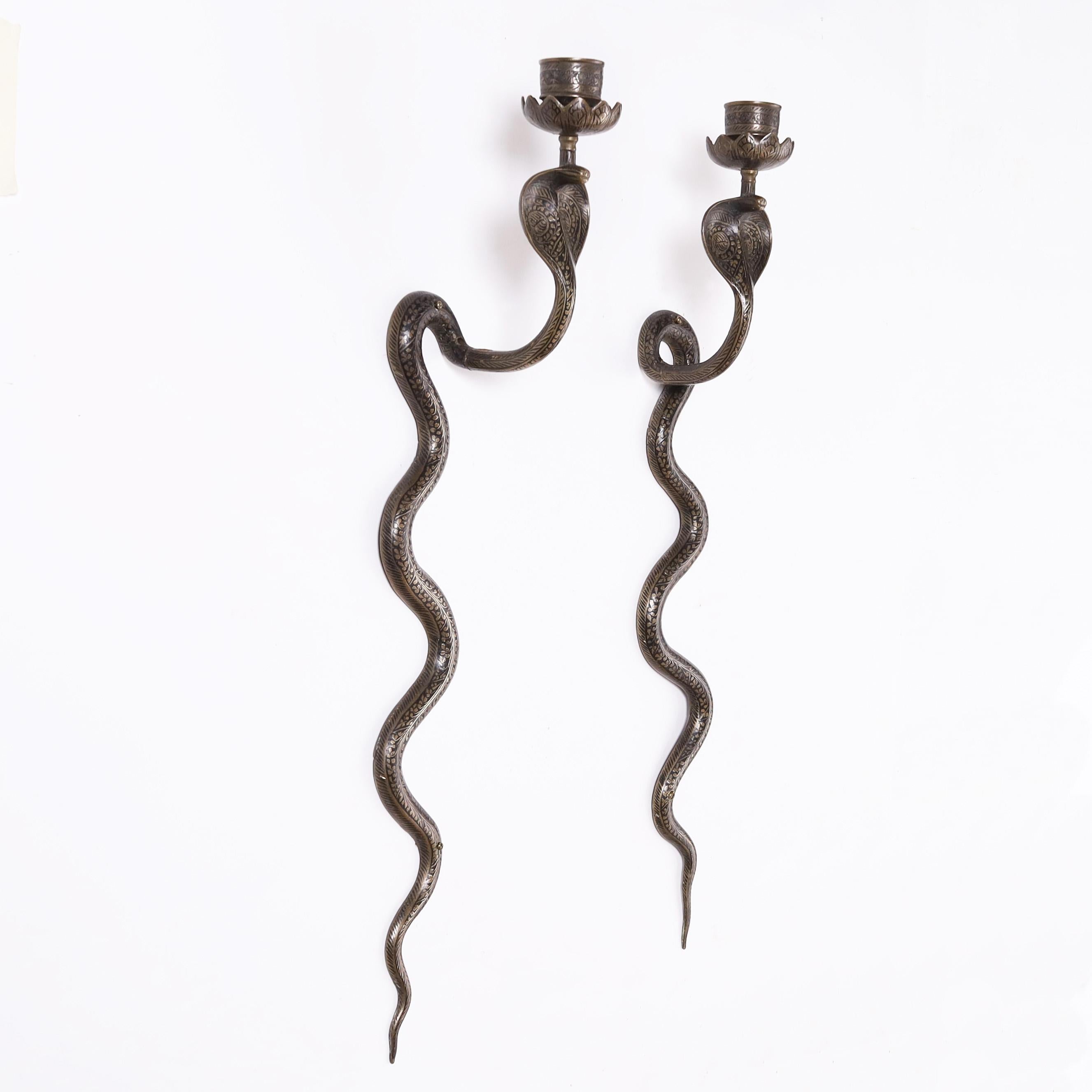 Standout pair of vintage Anglo Indian cobra or snake wall sconces crafted in brass with etched floral and geometric designs highlighted in black enamel and having an overall bronze like patina. 