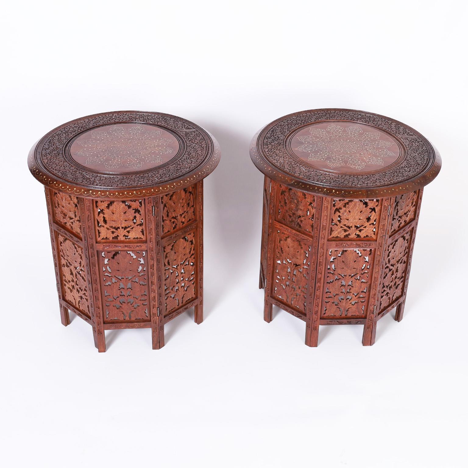 Impressive pair of Anglo Indian stands crafted in mahogany with round tops having brass string inlays in a center medallion with emanating floral designs inside elaborate leaf carvings. The octagon bases have carved leaves in open fretwork.