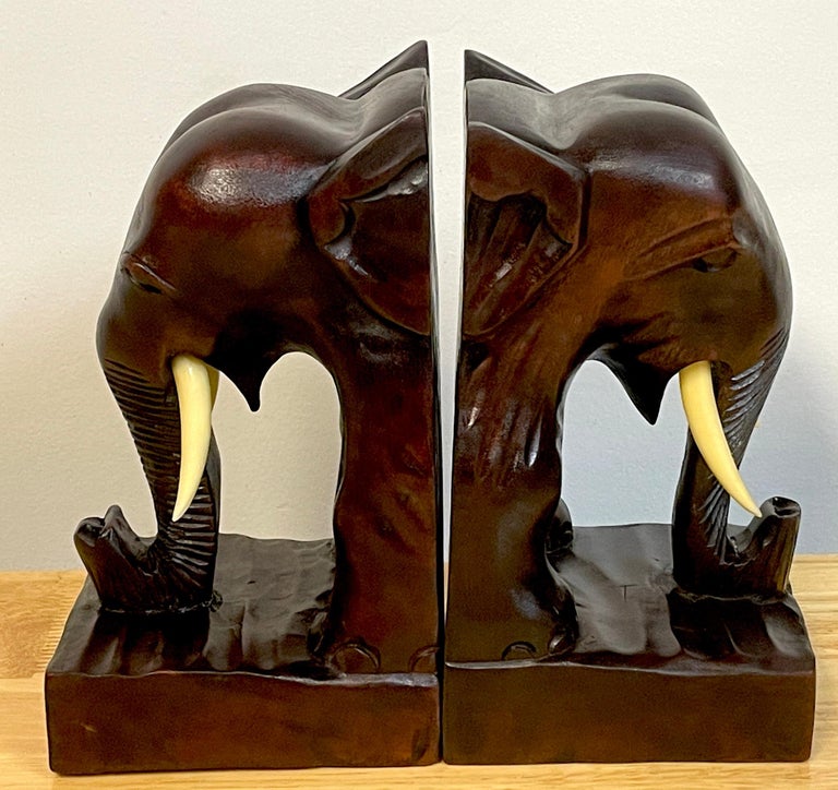 Pair of Anglo-Indian carved teak elephant bookends 
A stately pair of hand-carved Anglo-Indian elephant bookends. This mid-century, handcrafted portrait pair with carved bone tusks with upturned trunks, resting on 4.5-Inch square bases. 
 
