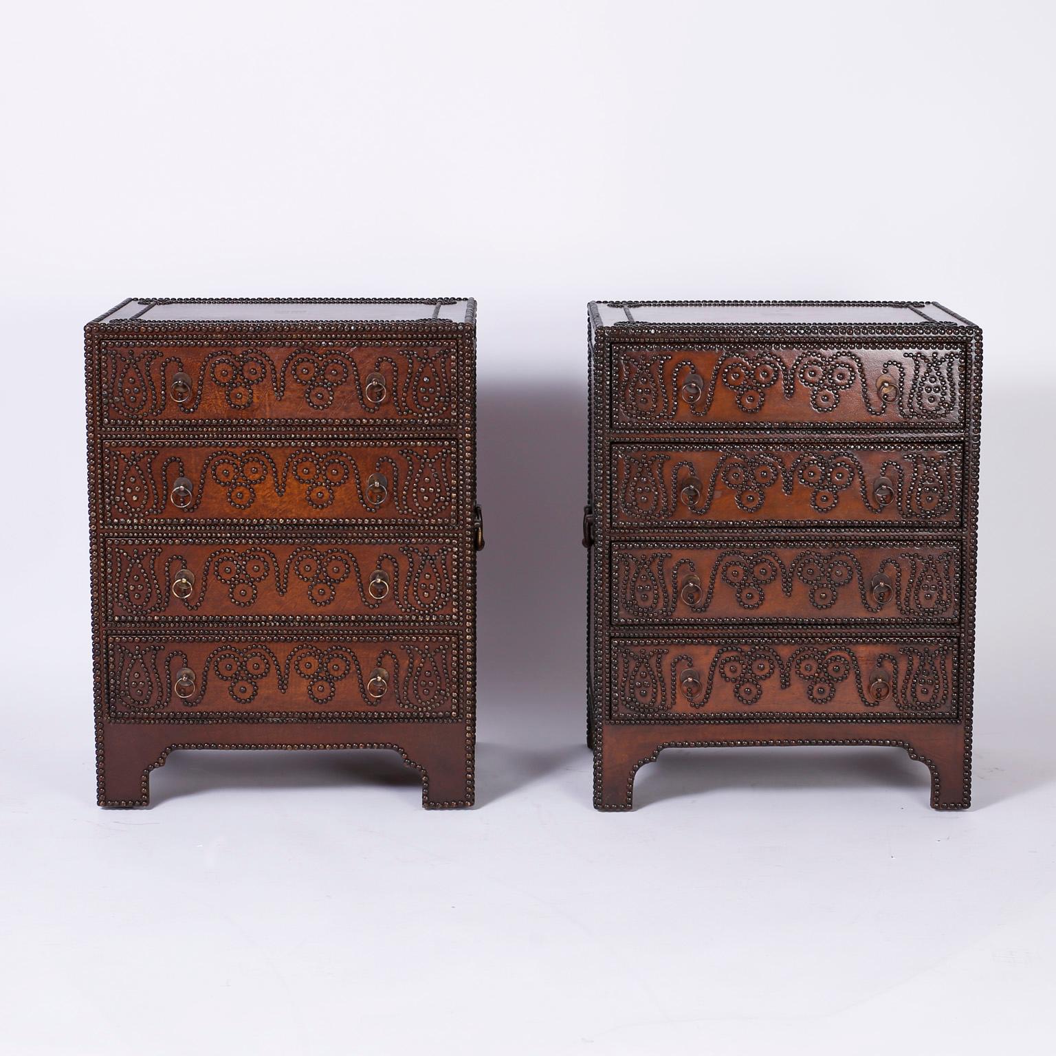Pair of Anglo-Indian brown leather clad chests with a unique display of studded floral and geometric designs on the top, front, and sides. The four drawer chests have side handles, confident stance, and modernized bracket feet.
