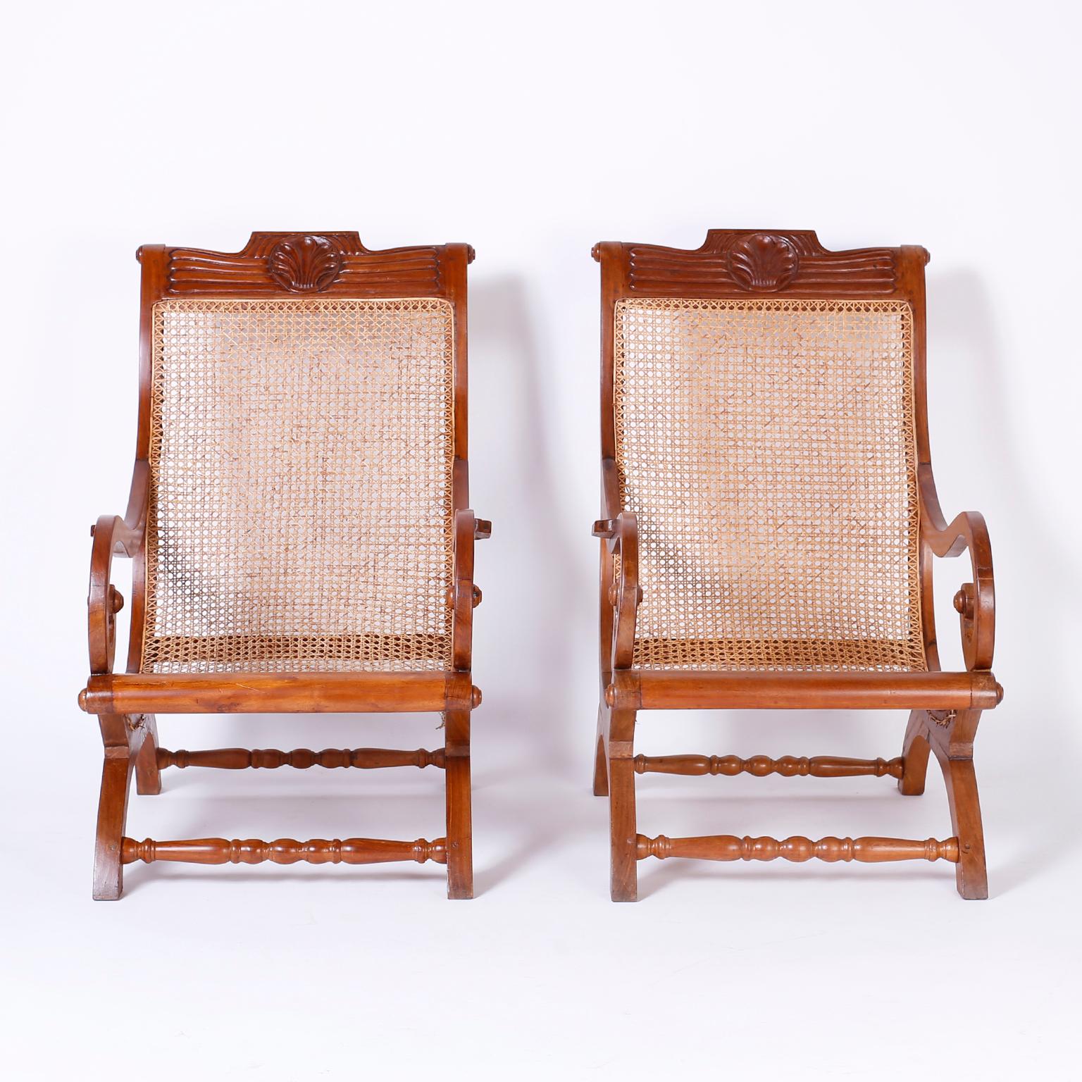Refined pair of antique Anglo Indian lounge chairs, hand crafted in mahogany. Detailed with a floral carved crest, caned back and seat, turned stretchers and a graceful flowing form.