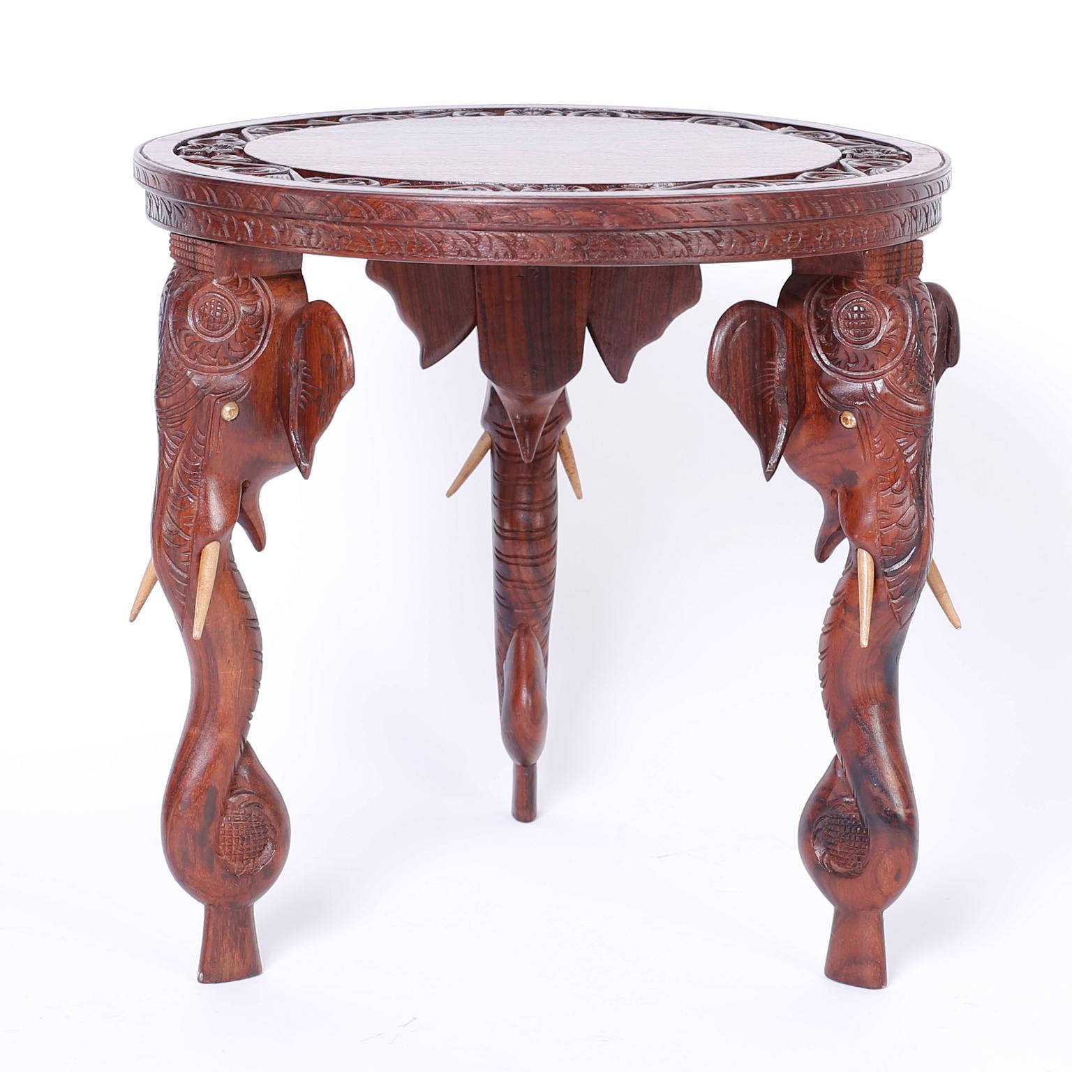 Exotic pair of Anglo-Indian round rosewood tables with carved floral borders on the tops and three carved elephant head legs with bone tusks.