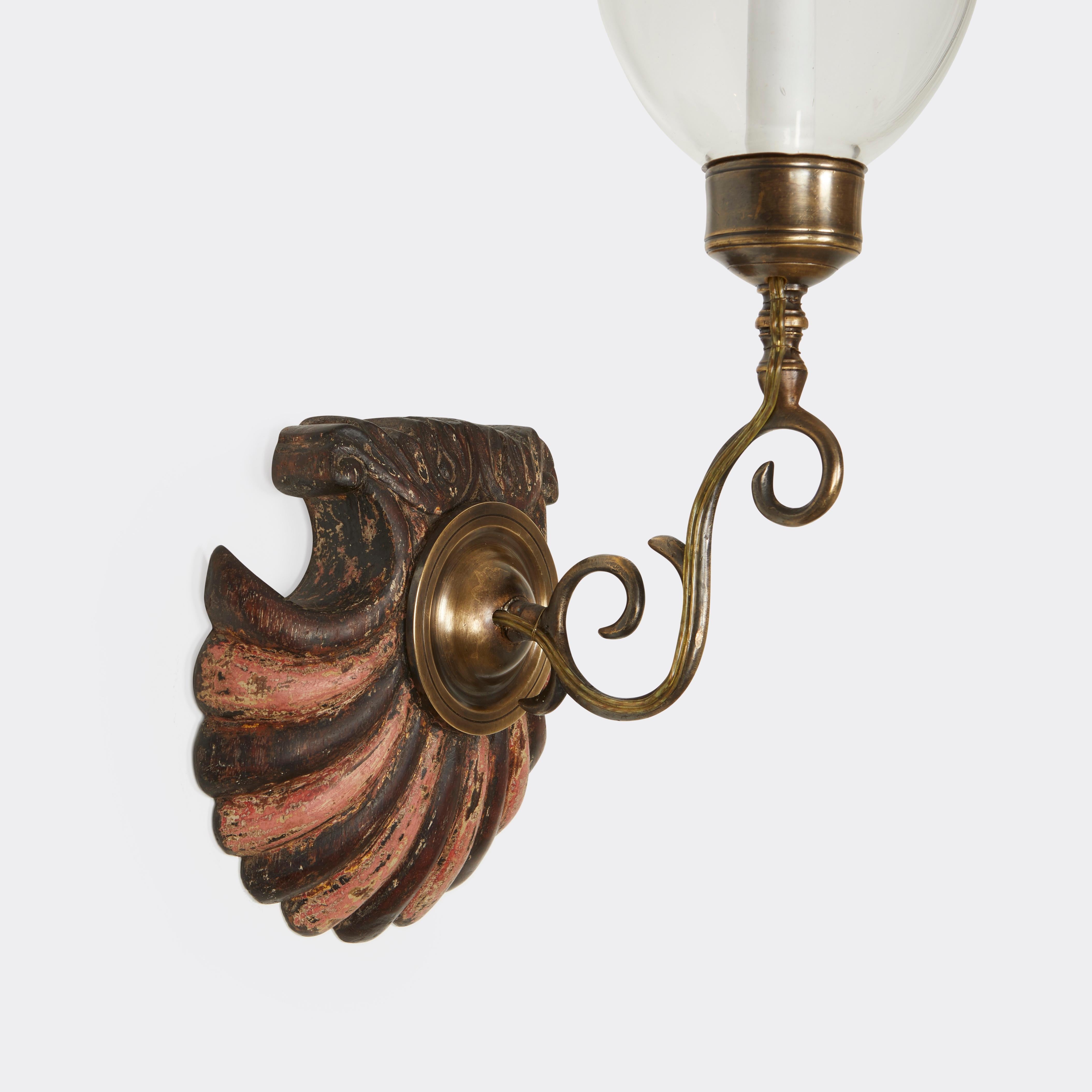 A pair of antique hand-carved scalloped shells from mahogany Anglo Indian styled backplates with painted decoration with pink stripes alternating with mahogany, patinated brass sconce fittings, and hand-blown clear glass. Electrified with one
