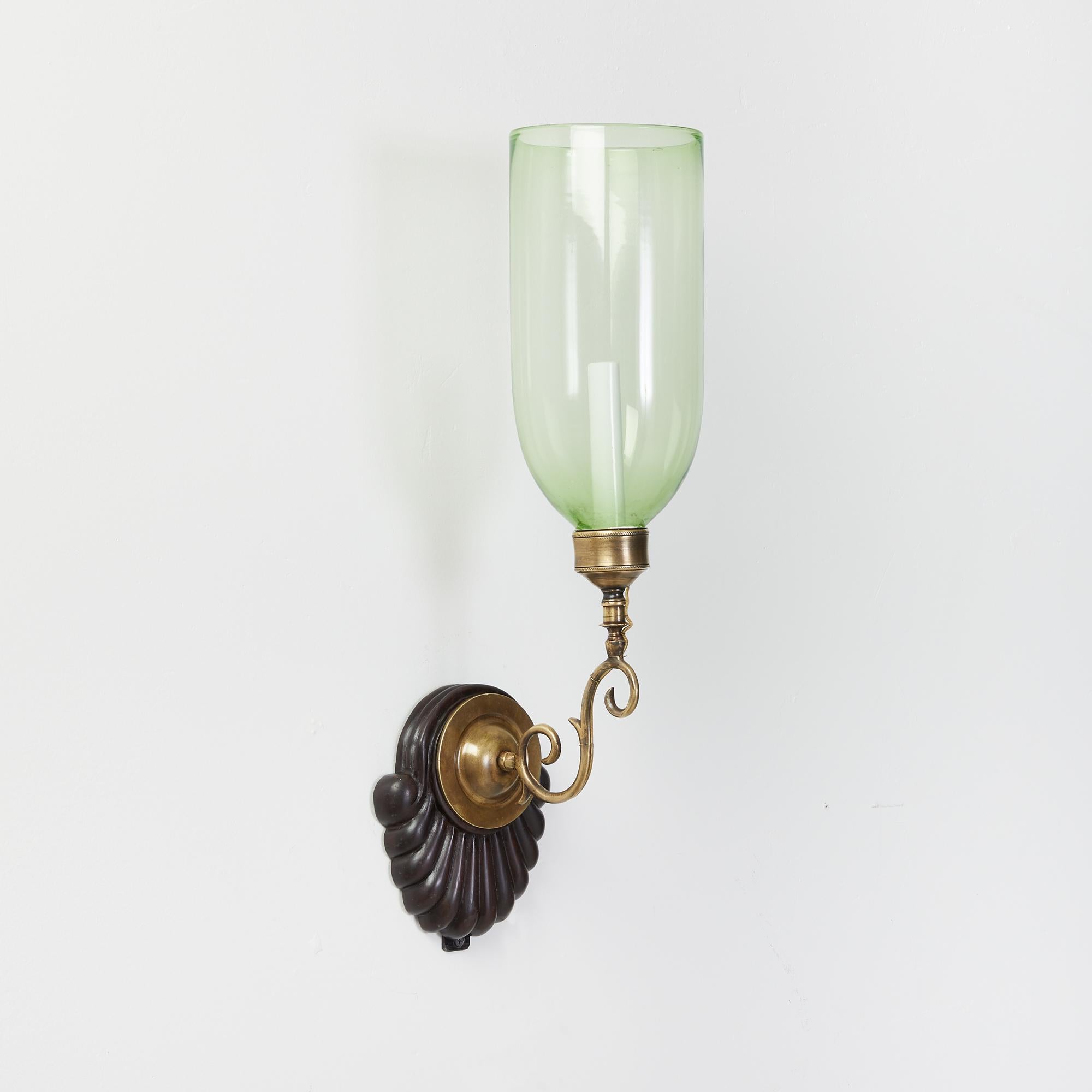 A pair of antique hand-carved shell form mahogany Anglo Indian backplates with patinated brass sconce fittings and light green glass hurricane shades. Electrified with one candelabra base socket per sconce.

Our custom hurricane sconces are
