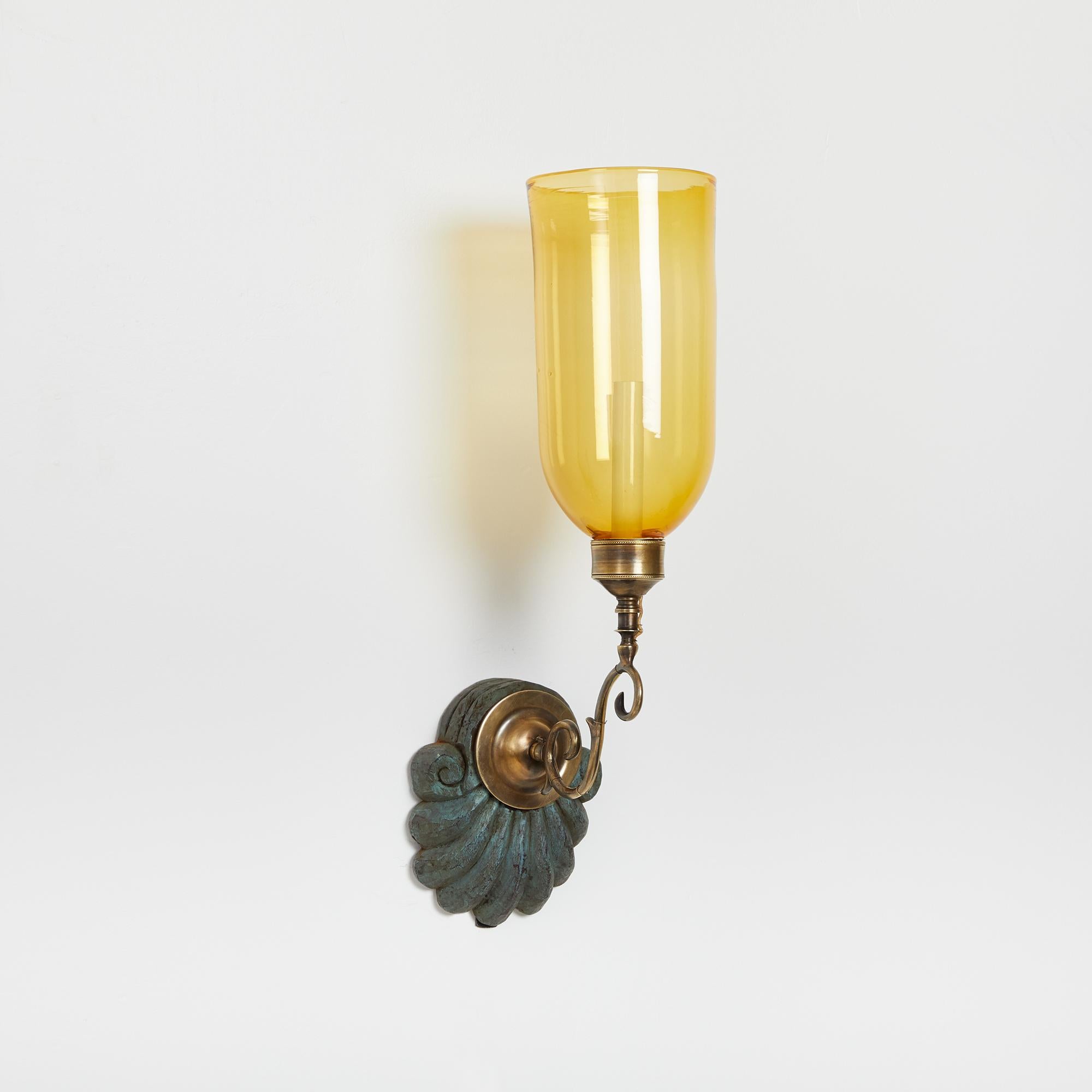 A pair of antique hand-carved shell form mahogany Anglo Indian styled backplates with verdigris finish, patinated brass sconce fittings and yellow glass hurricane shades. Electrified with one candelabra base socket per sconce.

Our custom hurricane