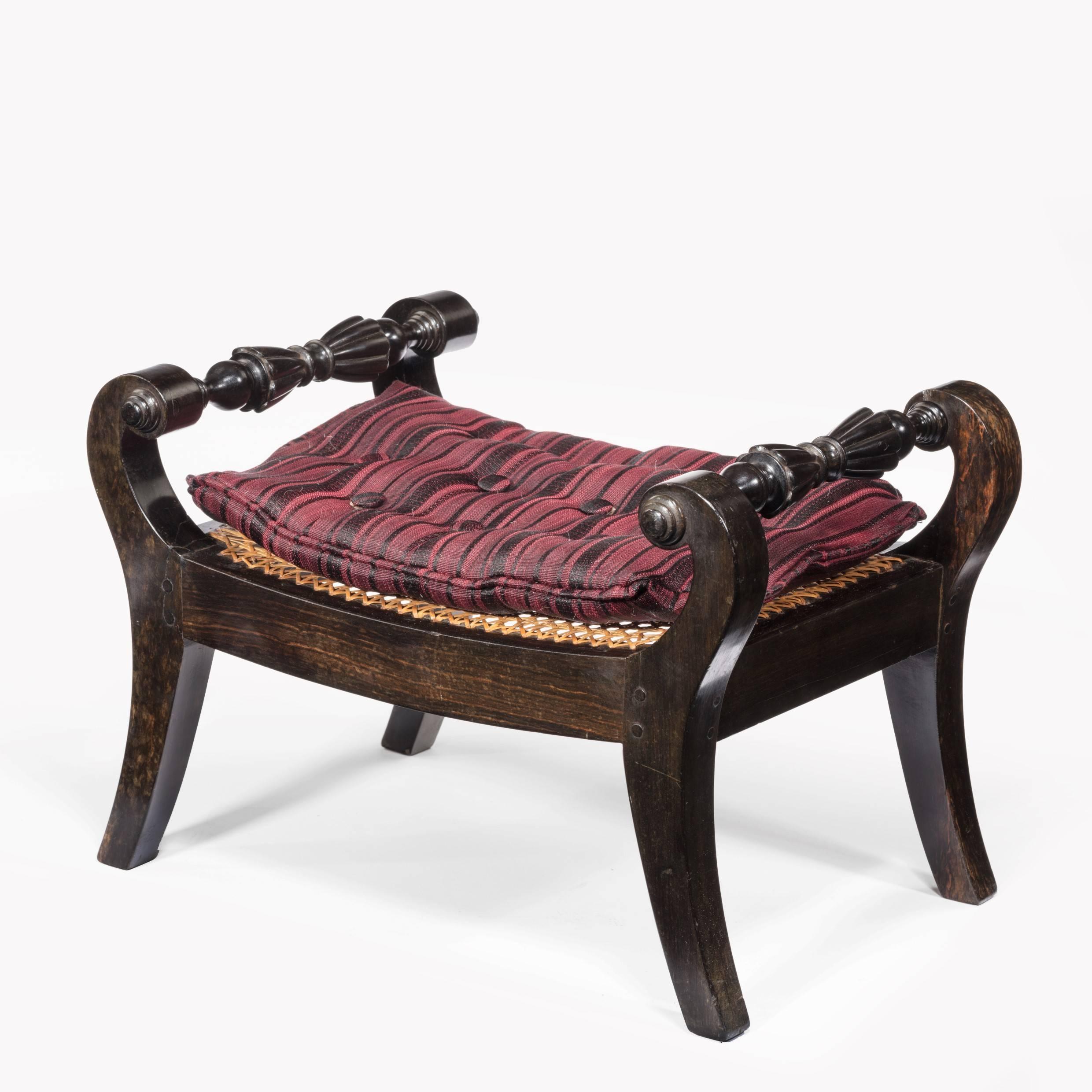 A pair of Anglo-Indian solid ebony footstools, each with two scrolling and reeded rails, cane seats and later cushions, circa 1810.