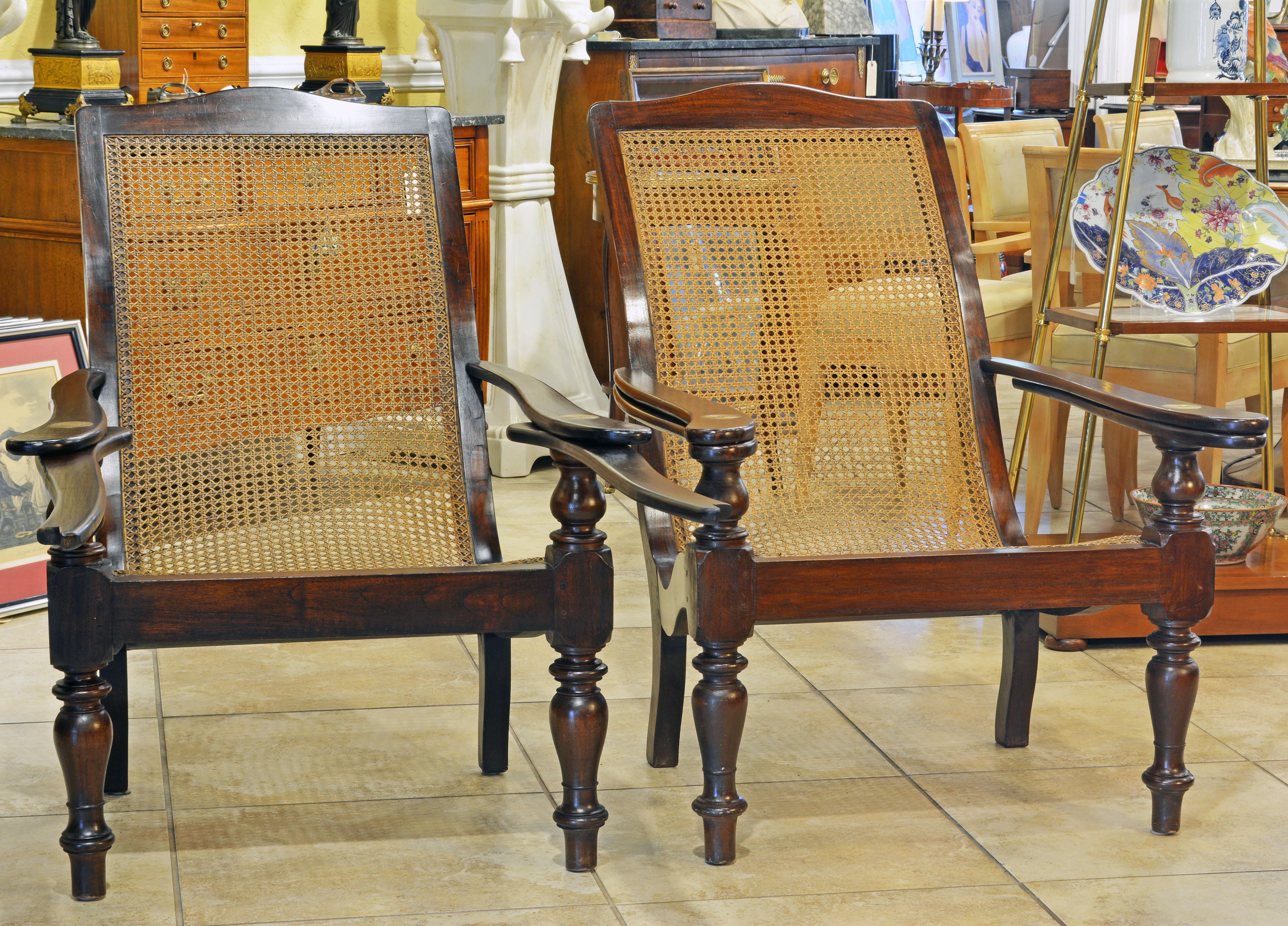 A charming and very British colonial pair of plantation or planter's chairs made of solid mahogany with decorative turnings and with caned seat and back in good condition. Part of the arrests swings out to form comfortable foot rests, all in the