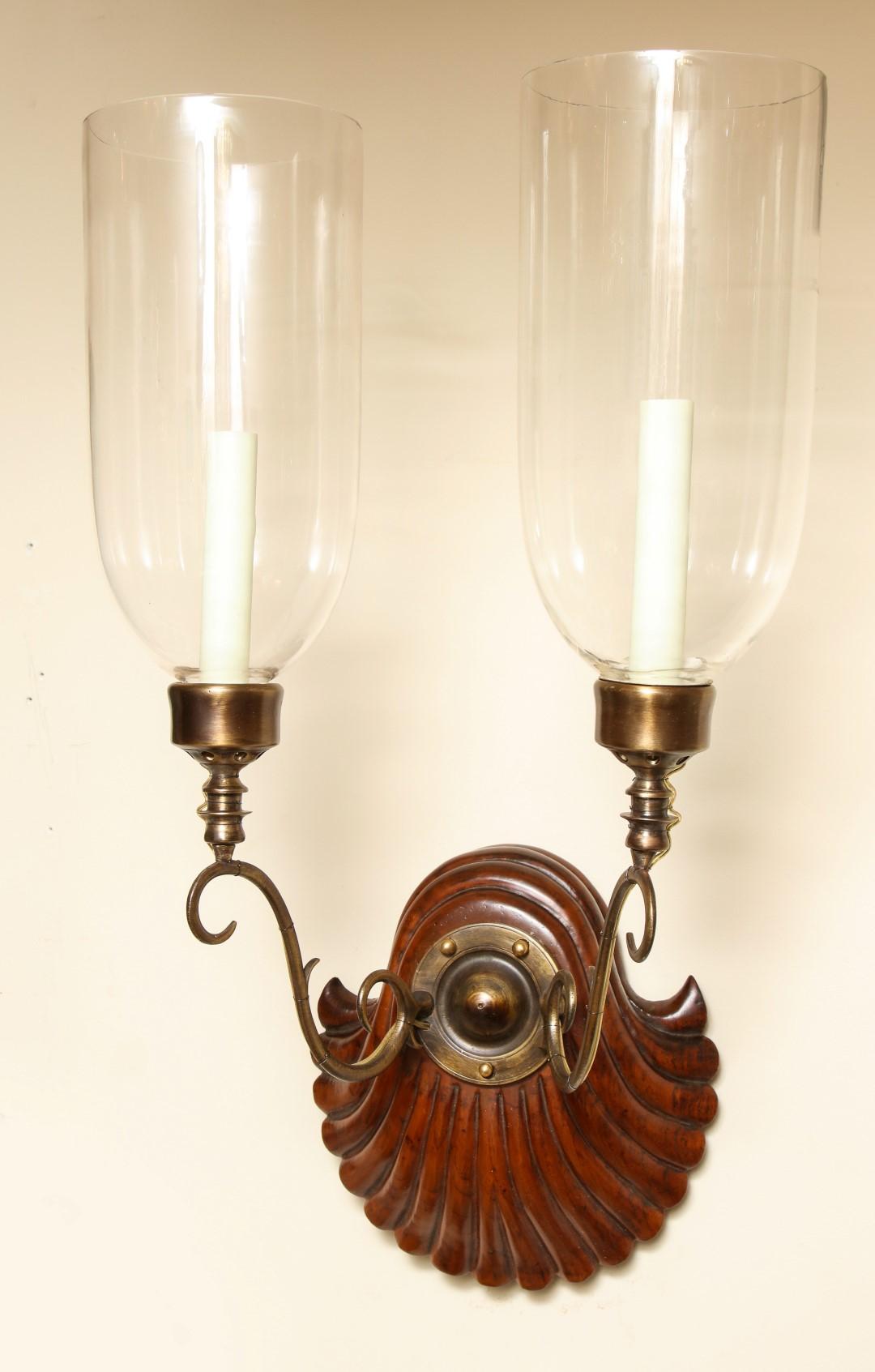 A pair of Georgian-style two-light sconces, hardwood shell form back-plate issuing bronze out-scrolled candle-arms supporting a single candelabra socket with hurricane shade. Maximum wattage per socket 60.

Our custom hurricane sconces are available