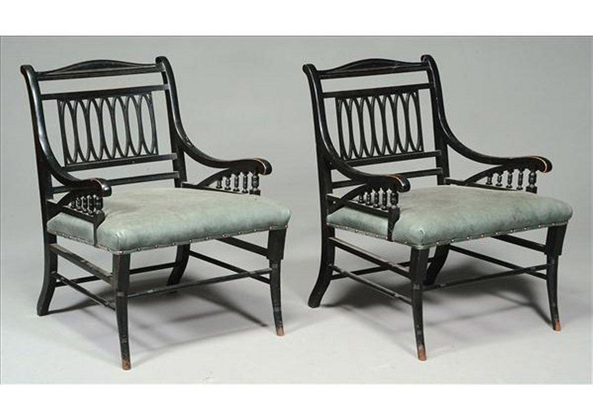 A pair of Aesthetic Movement ebonized open armchairs, Attributed to Jas Shoolbred with repeated elliptical backs, graduated spindles to the arms, re-upholstered leather seats and ring-turned out swept feet. Professionally reupholstered in a quality