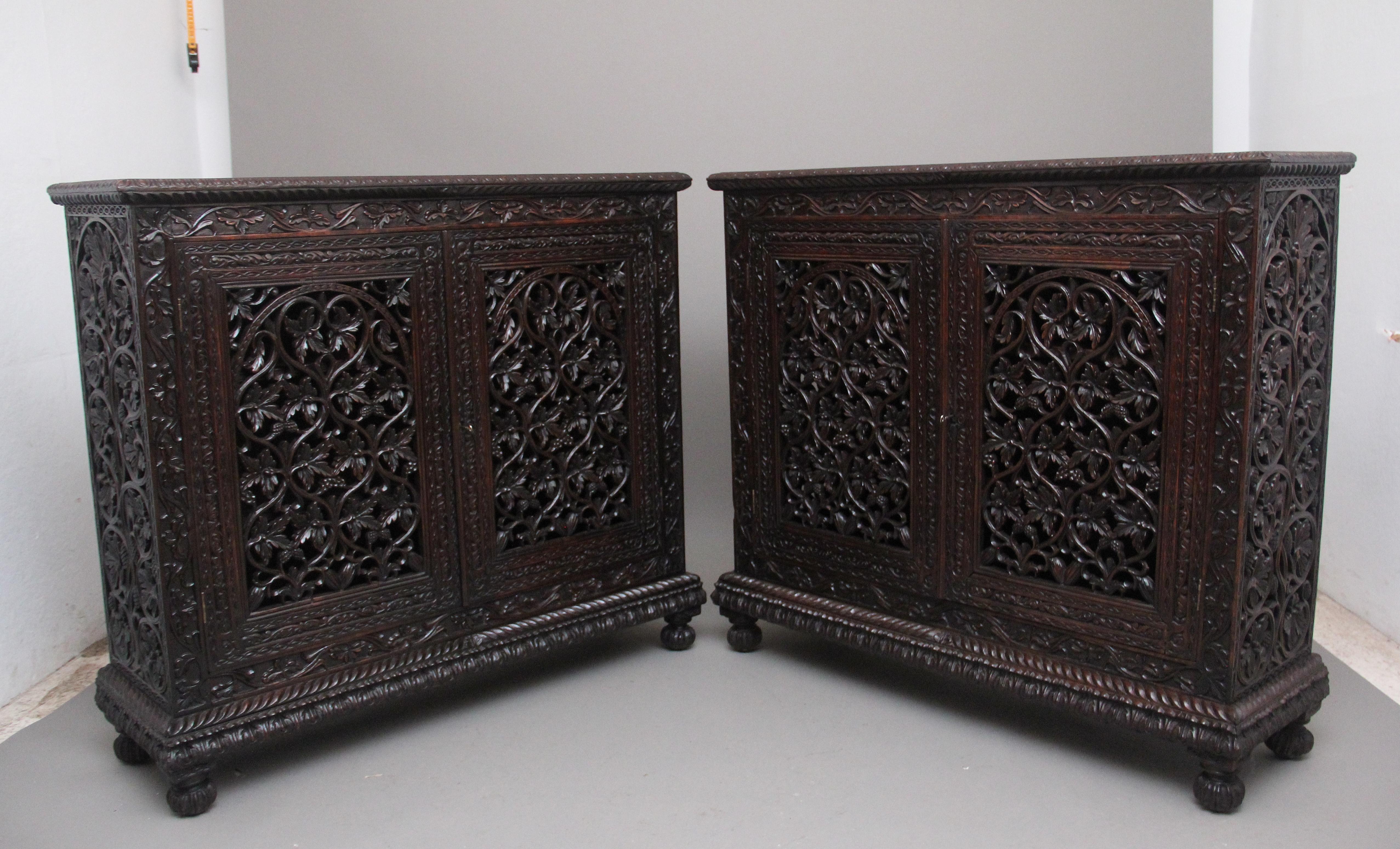 A stunning pair of antique 19th Century Anglo-Indian carved cabinets profusely carved throughout, having a lovely figured top with a decorative carved gadrooned edge above two hinged carved and pierced cupboard doors opening to reveal two shelves