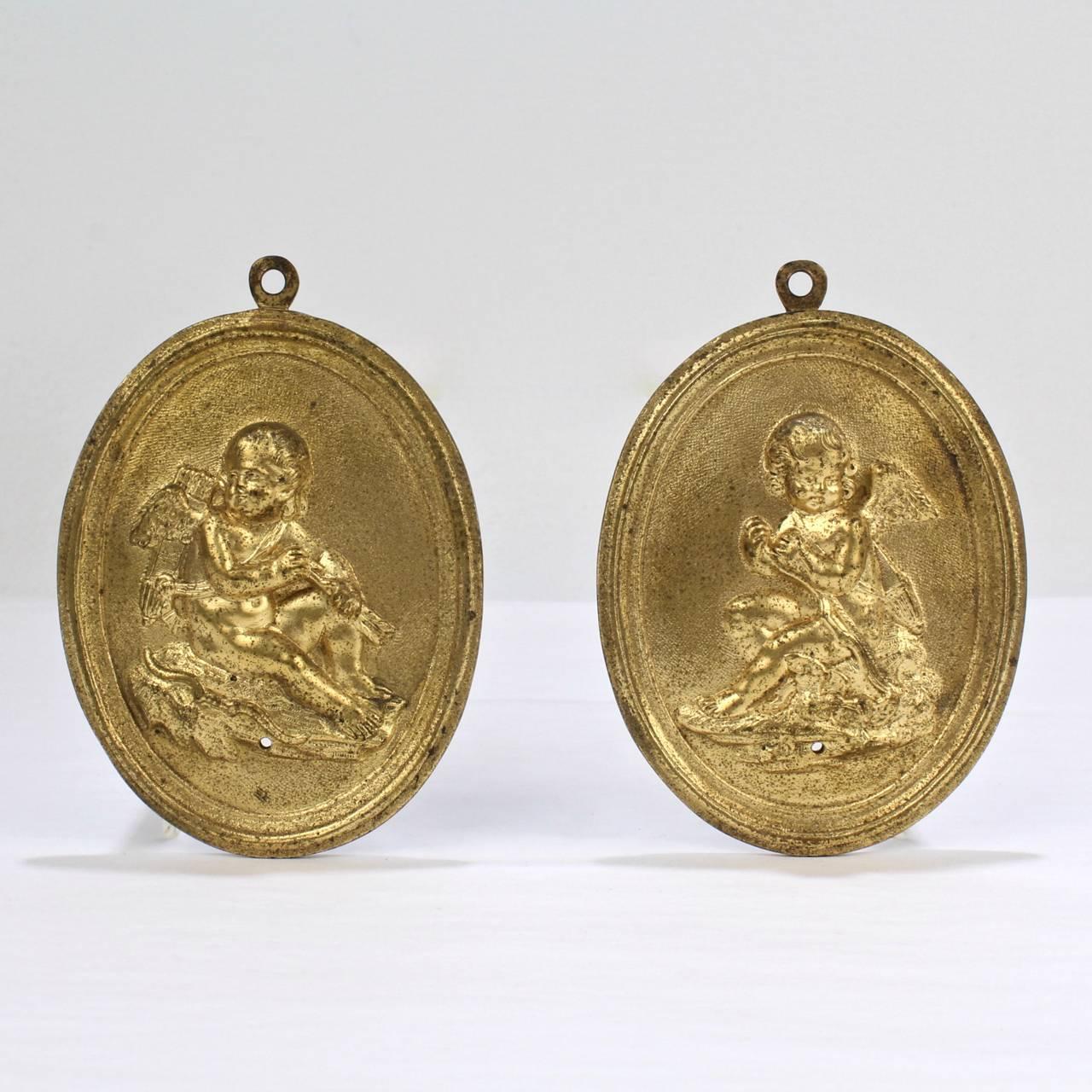 A fine pair of antique French bronze plaques depicting Cupid with his bow and arrows.

Of oval form with figural reliefs and a doré gilt bronze finish. The top with a small, cast attached bail for mounting.

Height: ca. 4 1/2 in.

Provenance: