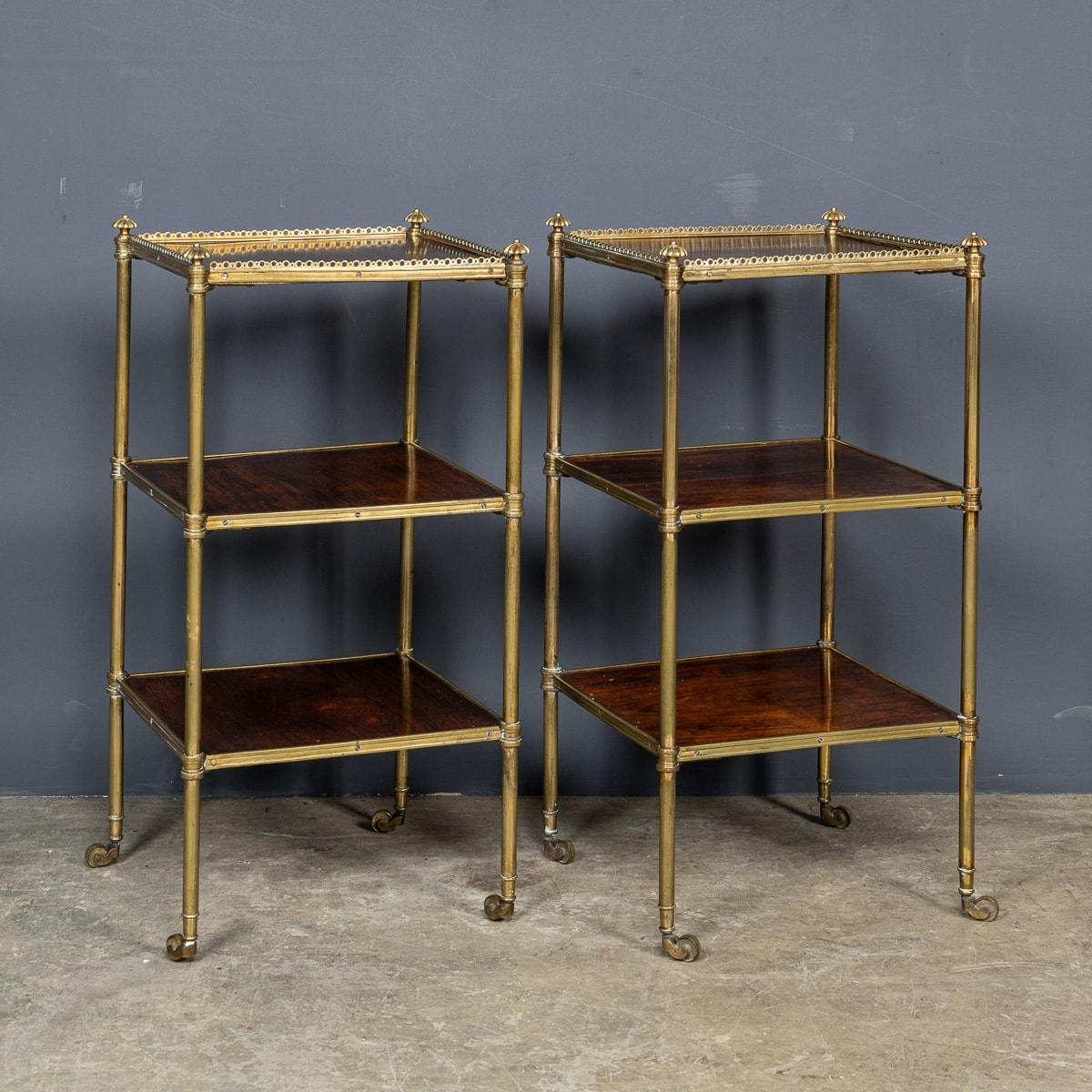 Antique 19th Century pair of Regency rosewood & brass etageres. This pair showcases a brass pierced upper gallery, harmonising with three tiers of square-shaped rosewood shelves, upheld by a tubular brass frame. Enhanced with cast roller wheels,