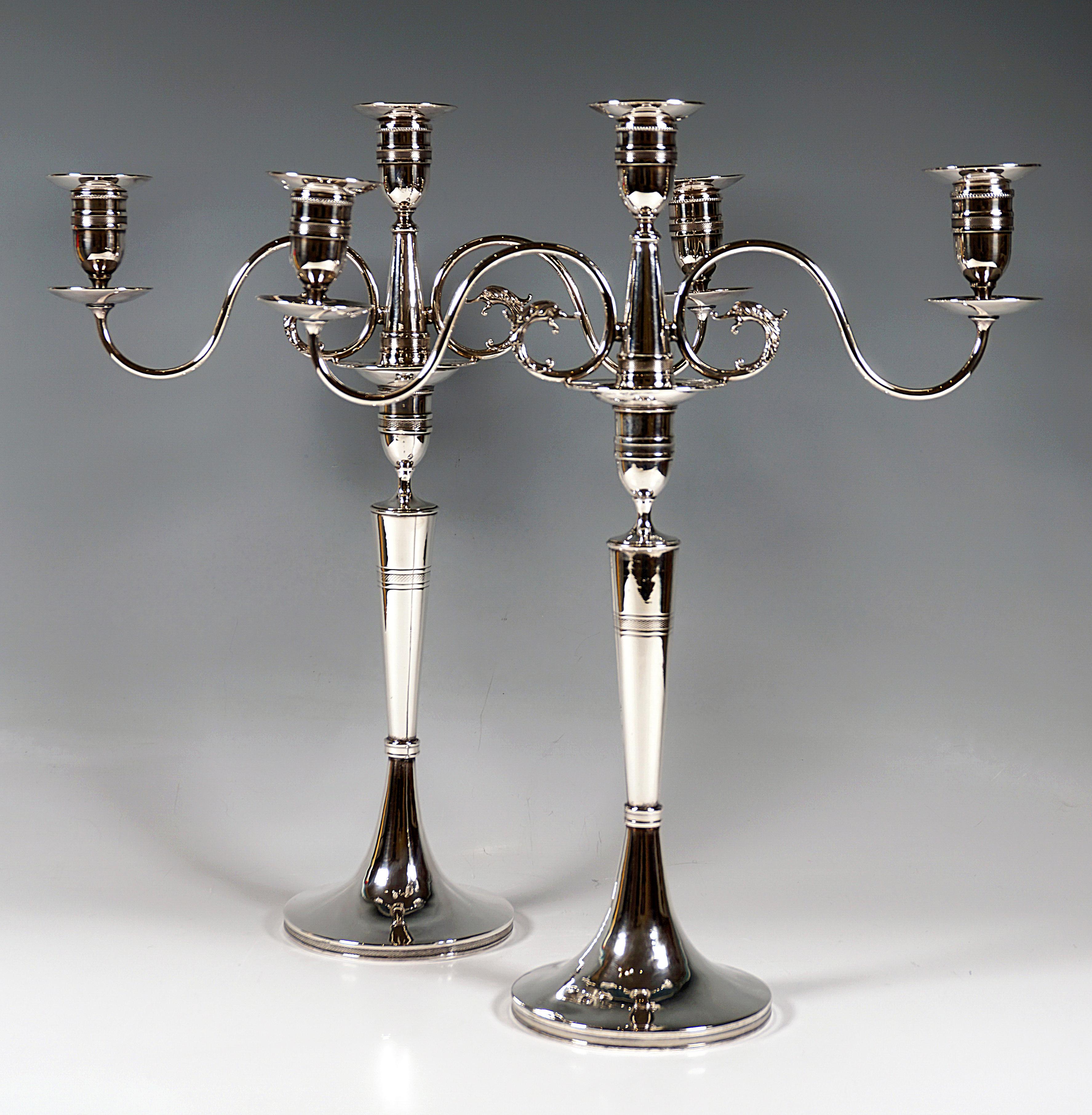 Two elegant 3-flame silver girandoles on a round base, smooth shaft raised in the centre, the lower third constricted by a profiled beaded ring, the shaft widening conically towards the top, a vase-shaped spout on top as a holder for the top piece