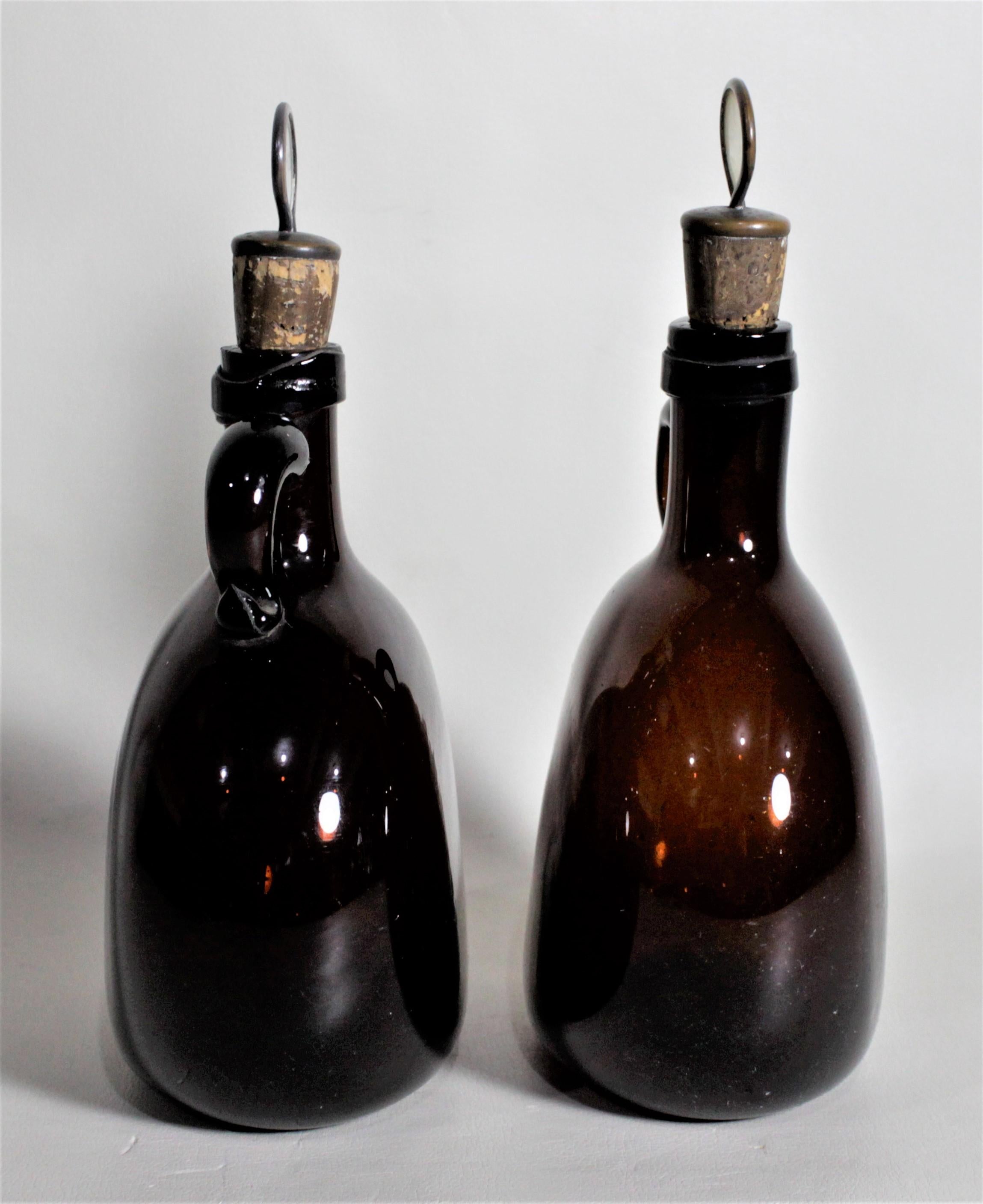 This pair of antique amber blown glass bottle flasks, or decanters were made in circa 1870 in the period Victorian style and originate from England. These decanters are hand formed, so not perfectly identical and have swirled finger handles and a