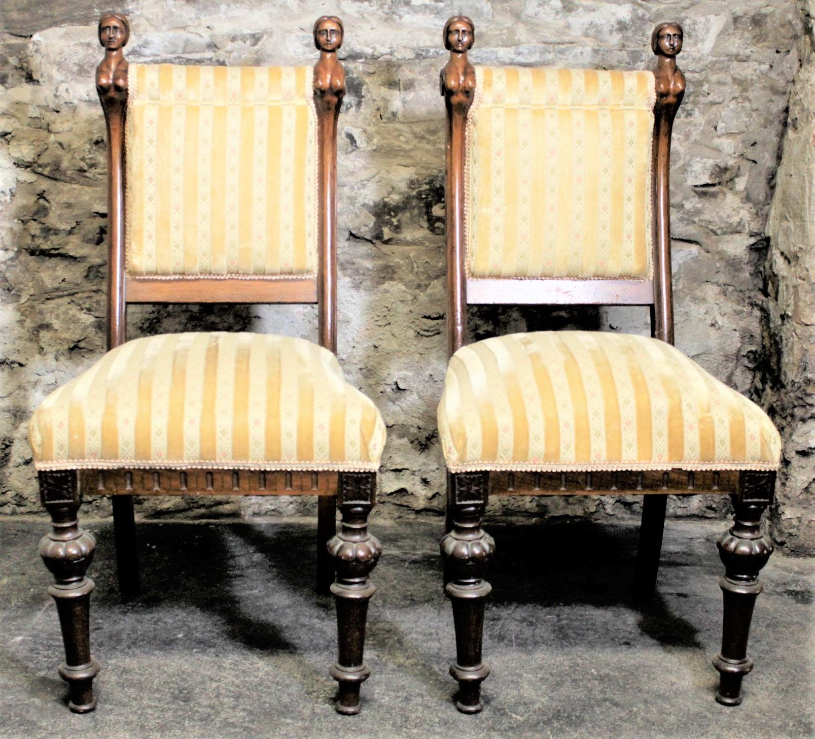 This pair of antique chairs is unsigned but believed to have been made in the United States in circa 1880 in the Victorian style. The chairs have hand carved wooden frames and feature two ornately carved busty figural females with blank stares on