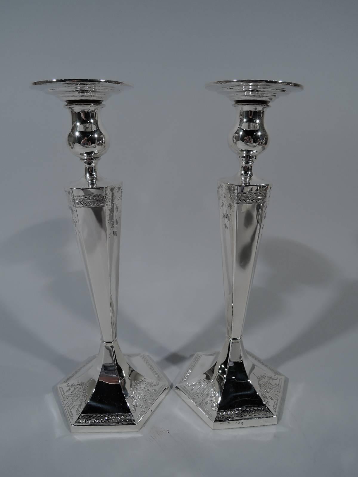 Pair of American Edwardian sterling silver candlesticks. Each: Tapering and faceted hexagonal shaft, raised hexagonal foot, and bulbous socket with wide and stepped detachable bobeches. Engraved stylized ornament: Leaves and flowers and imbricated