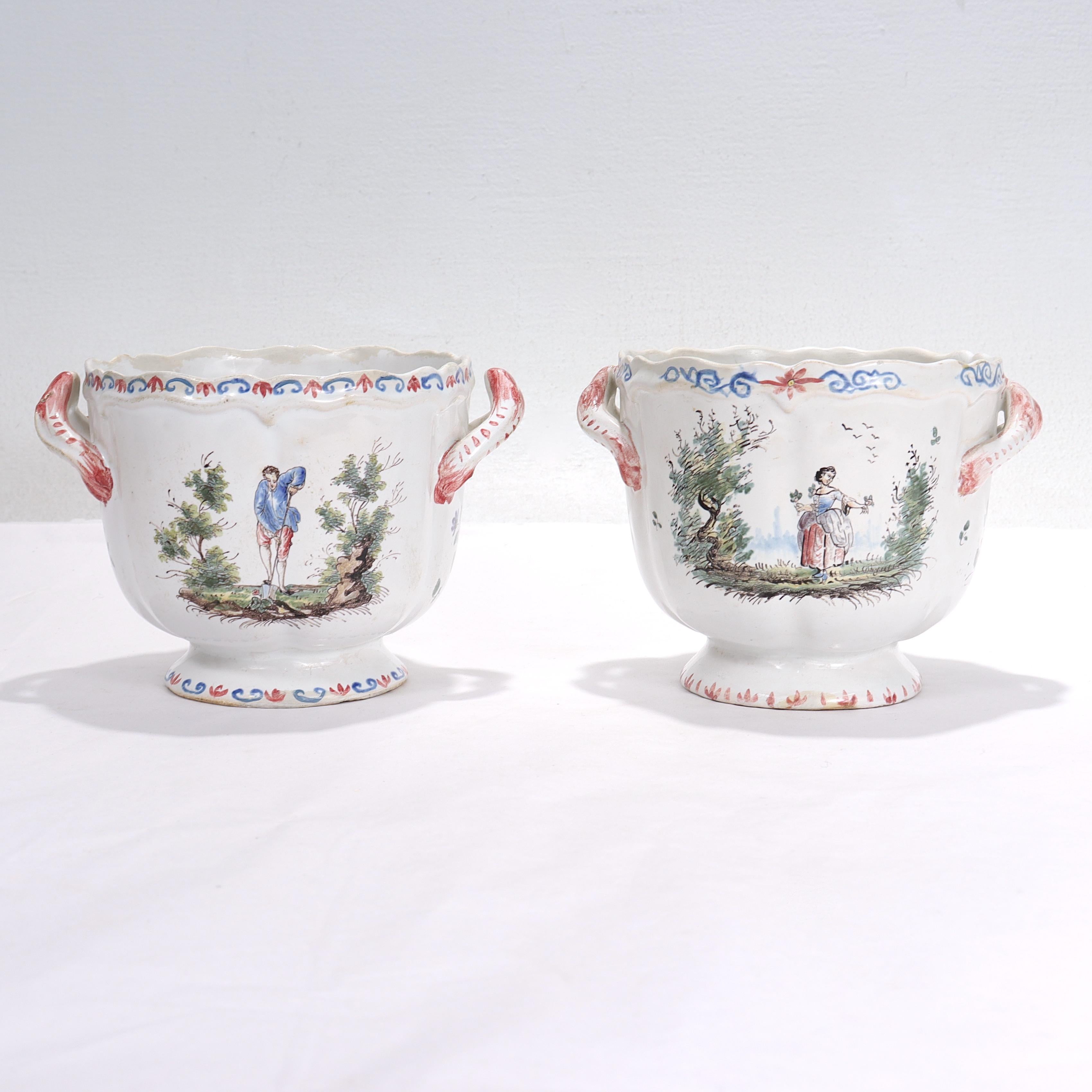 A fine pair of antique French faience jardinieres or cachepots.

By Aprey. 

Each with two painted scenes on either side. One has a man gardening and a woman carrying a breadbasket on her head, while the other has a woman holding flowers and a