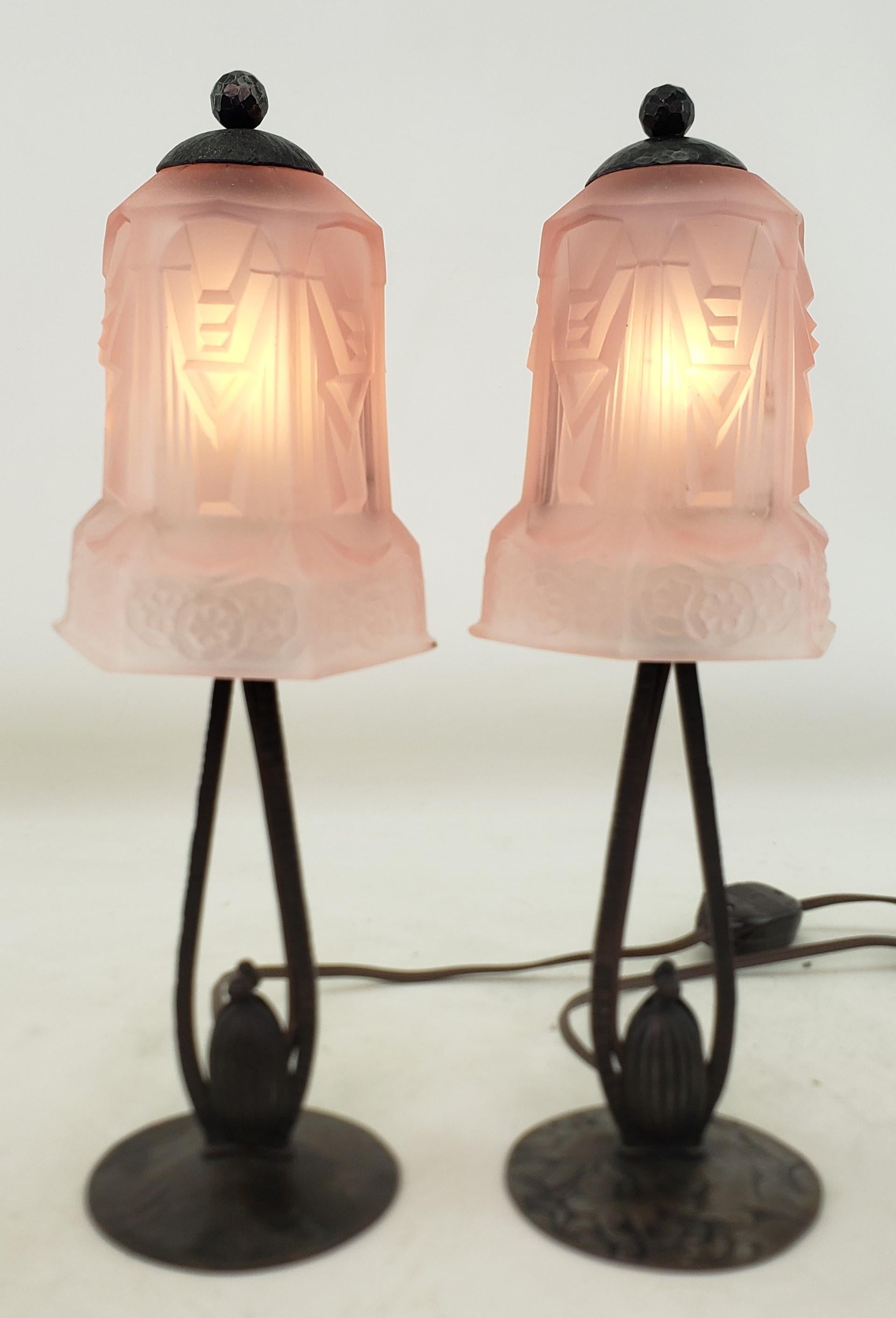 Dieses Paar kleiner antiker Tischlampen ist unsigniert, stammt aber vermutlich aus Frankreich und wurde um 1920 im Art-déco-Stil gefertigt. Die Lampenfüße bestehen aus bronzefarbenem, patiniertem Stahl und die Schirme aus dickem, geformtem rosa