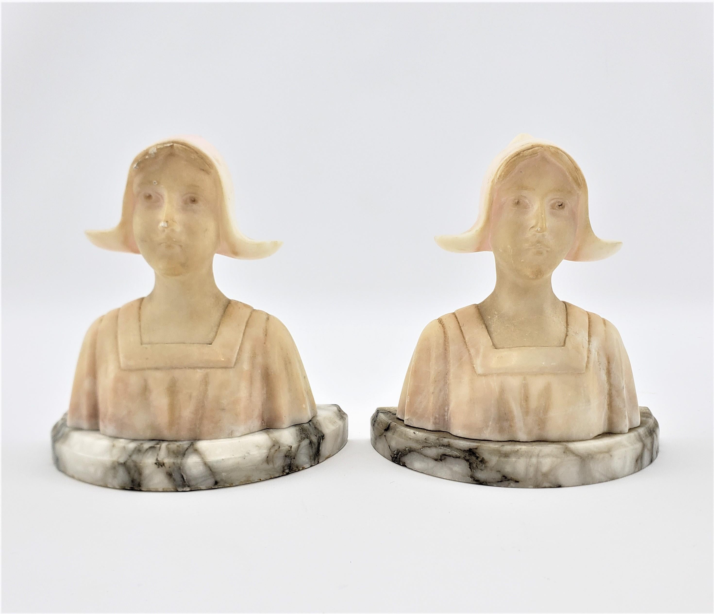 This pair of Art Deco bookends are unsigned, but presumed to have been made in the United States in approximately 1920. The bookends are composed of carved alabaster as miniature busts of maidens. The carved sculptures are set on half moon shaped