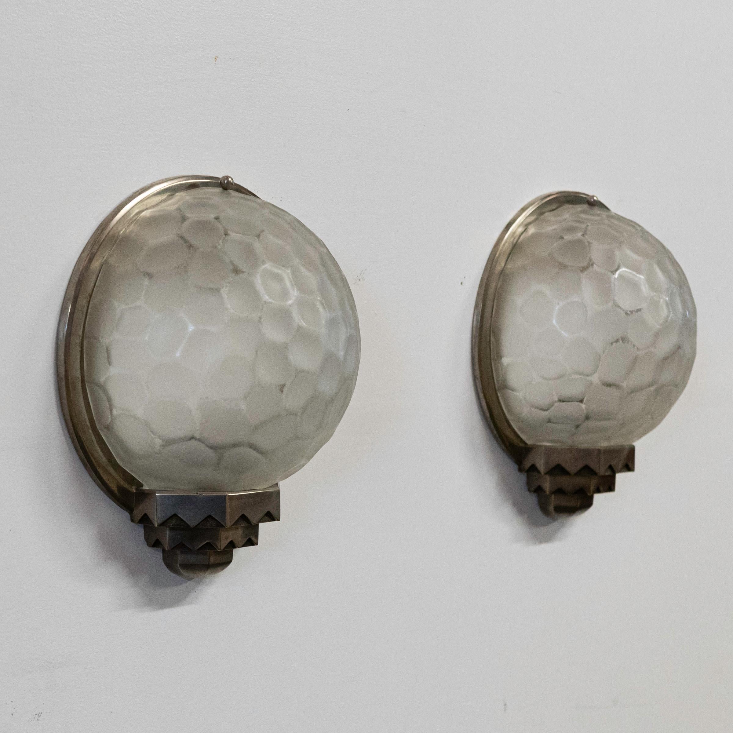 Inconfondibilmente Art Déco, queste applique in vetro pressato e modellato sono opera dei famosi designer Parison Philippe Genet & Lucien Michon.

Le luci originali dell'inizio del XX secolo sono incorniciate da una base geometrica e smerlata. La