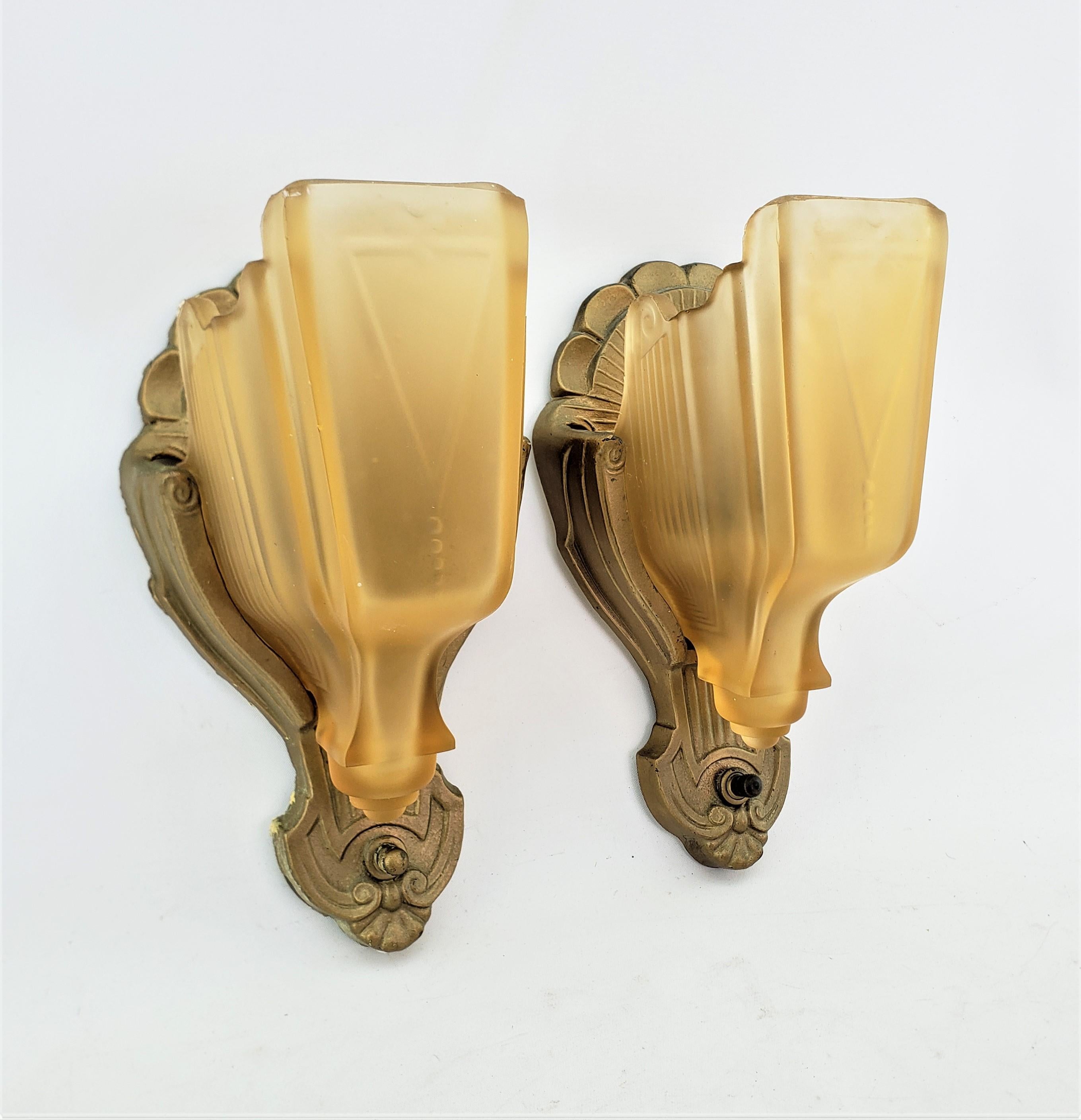 This pair of wall sconces were made are unsigned, but presumed to have originated from the United States and date to approximately 1920 and done in the period Art Deco style. The backing plates are composed of cast metal with a worn painted finish,