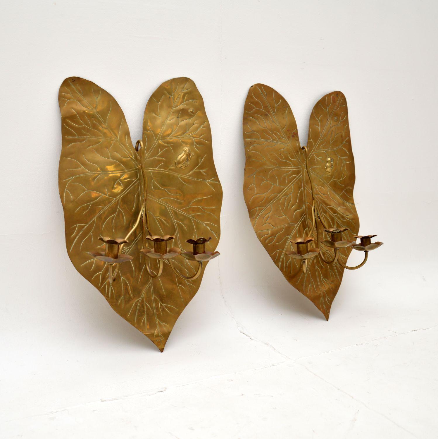 A stunning and quite unusual pair of antique Art Nouveau brass wall mounting candelabra. They were made in England, and they date from around the 1890-1900 period.

They depict large water lily leaves, each has a small frog in the top corner hunting