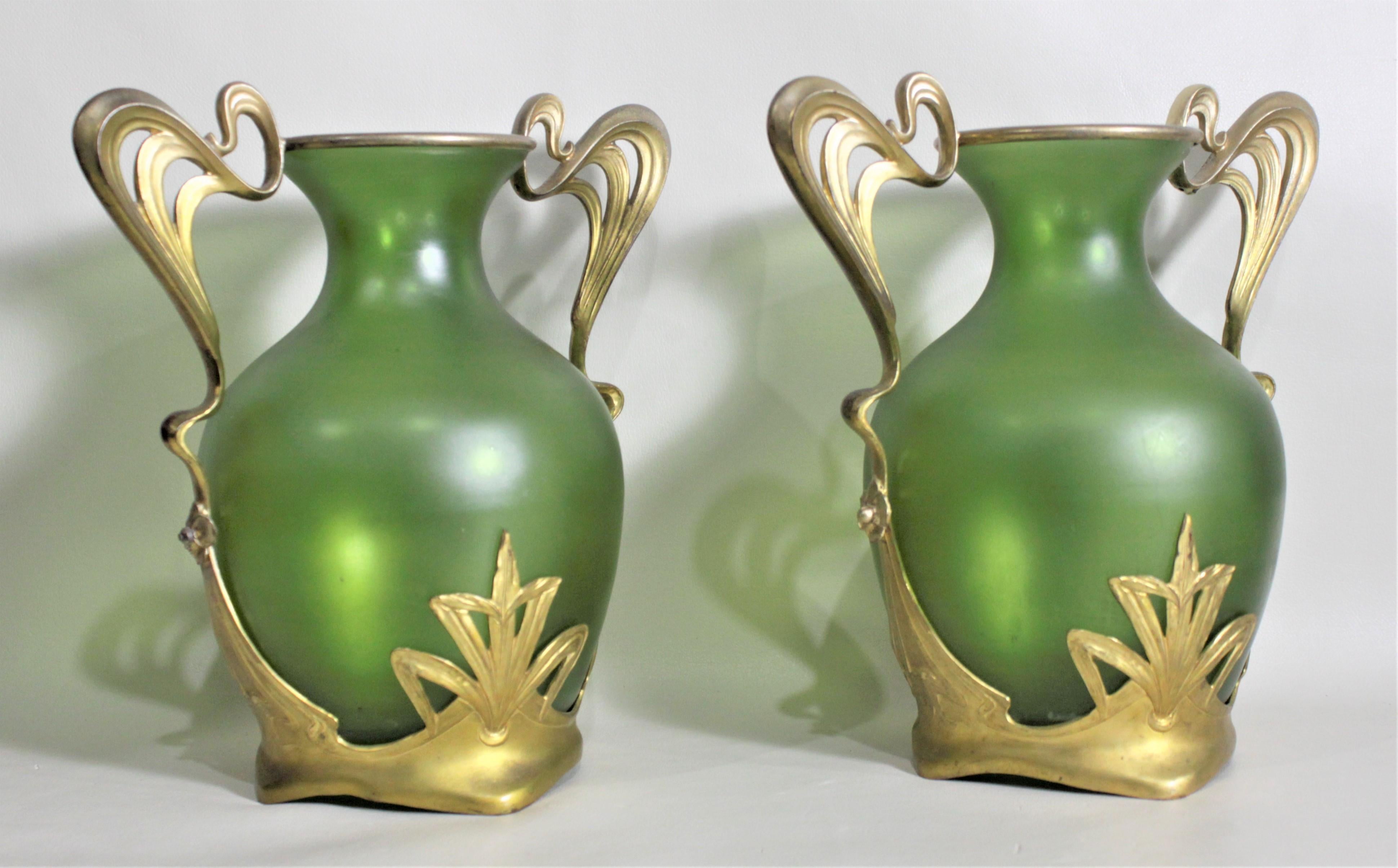 This pair of antique deep green art glass vases with gilt metal mounts are unsigned but presumed to have been made in Austria in circa 1900 in the period Art Nouveau style. The vases are done in a deep rich green which are framed by the bright gold