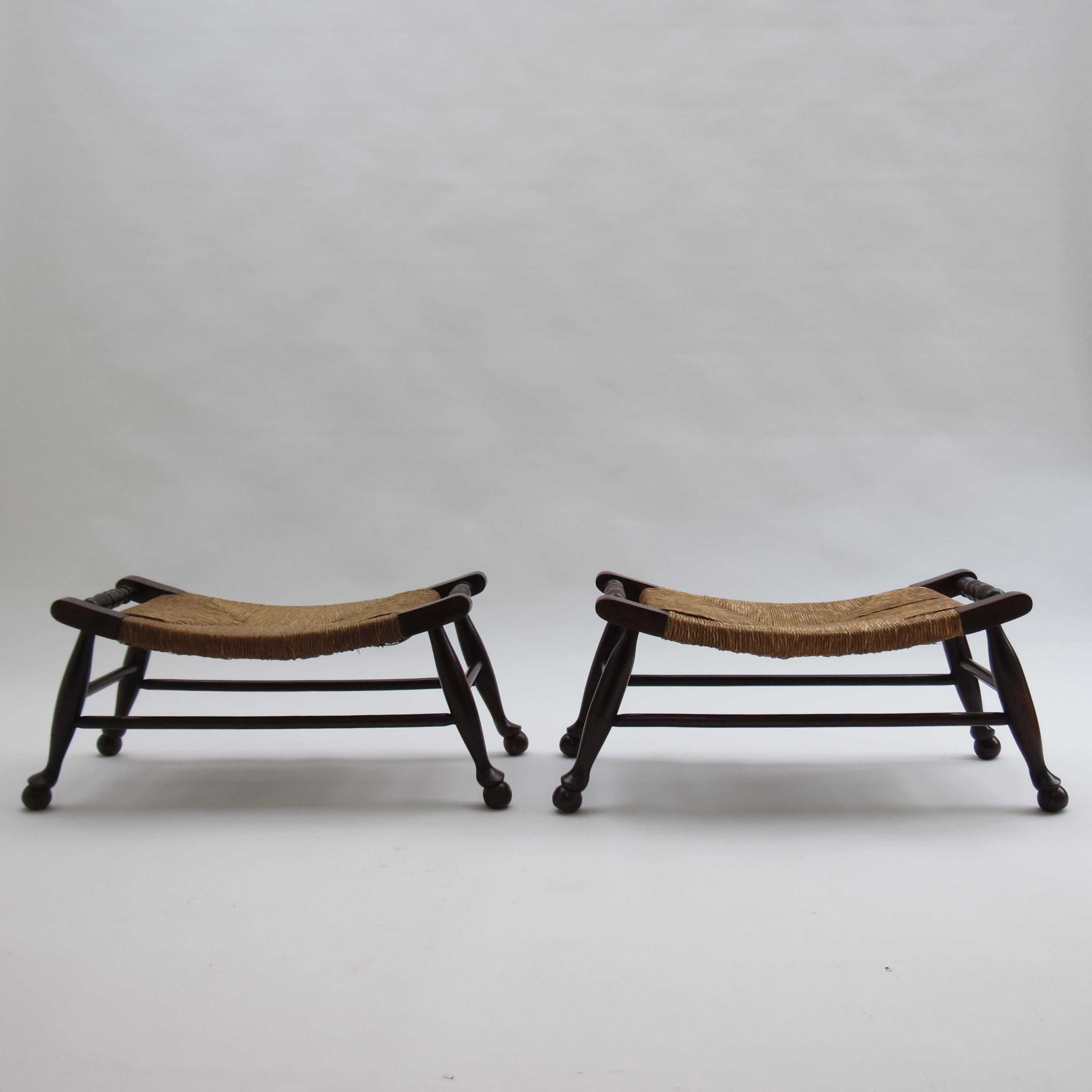 Wonderful pair of arts and crafts low slung stools. The frames are made from solid Oak and Elm and and retain the original coloured finish.  They date from the early 1900s.    Wonderful original rush seats.

In good over all condition. They have