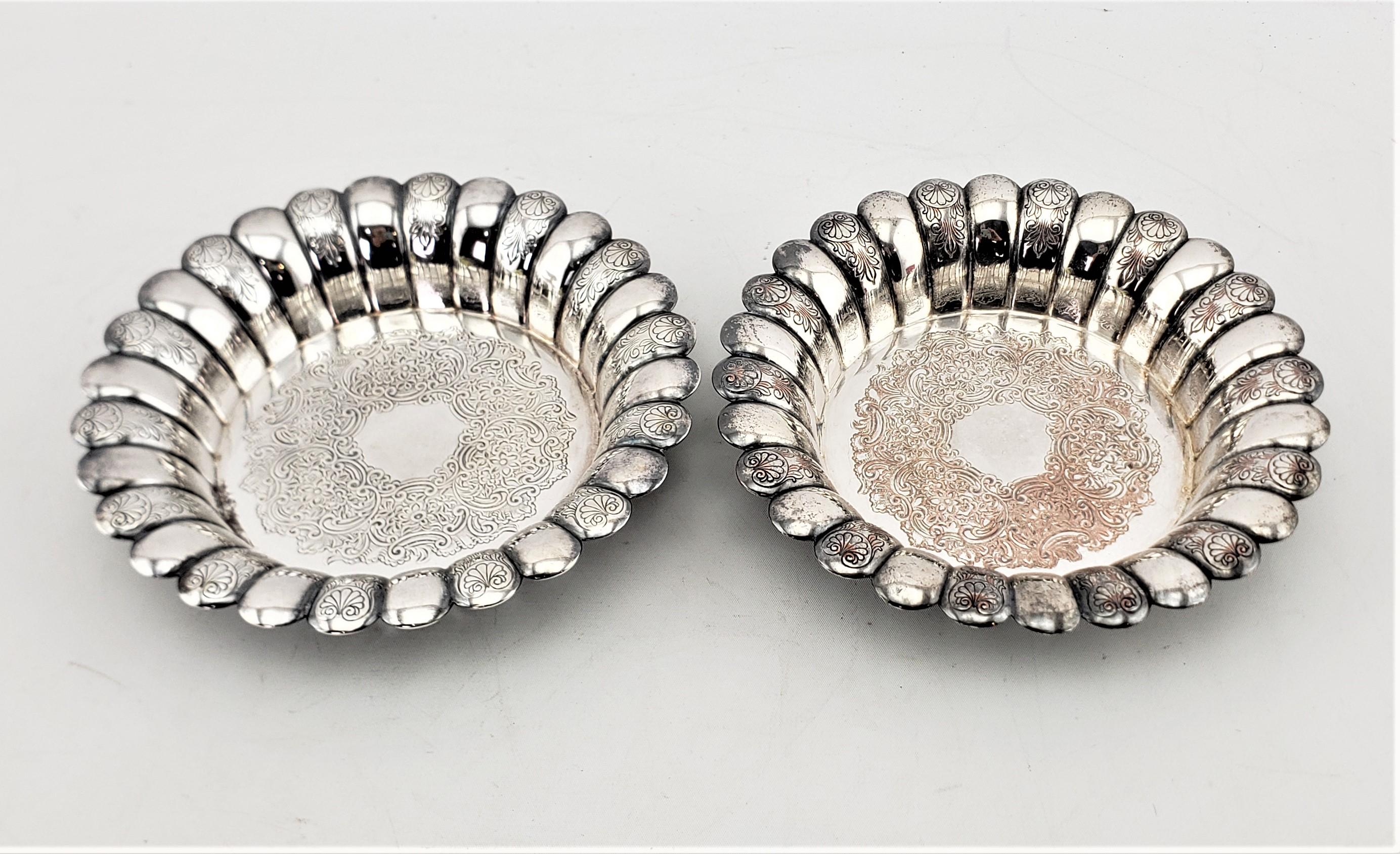 This pair of antique silver plated bottle coasters was made by the well known Barker-Ellis Silver Co. of England in approximately 1920 in an Edwardian style. The coasters are done with a curled scalloped edge with engraved stylized shells on