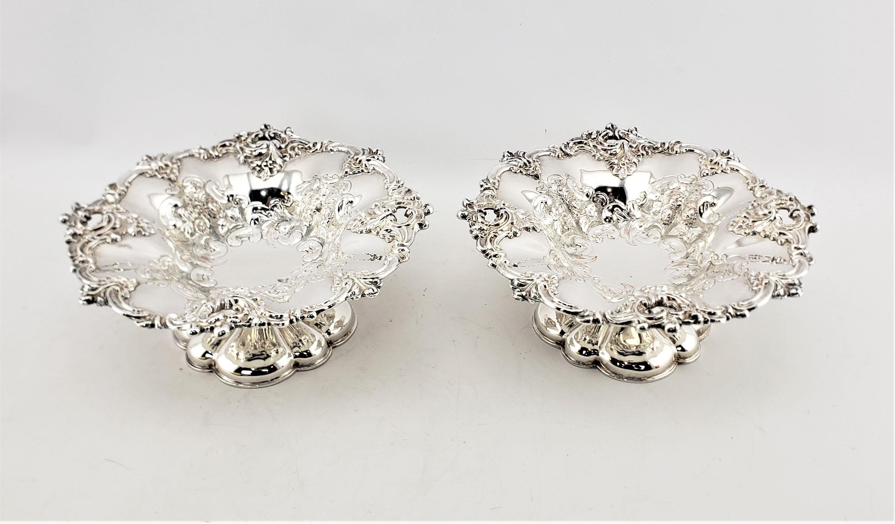 This pair of antique silver plated footed bowls or tazzas were made by the well known Barker-Ellis of England in approximately 1920 in a Victorian style. The bowls are done in silver plate over copper with scalloped edges with applied stylized