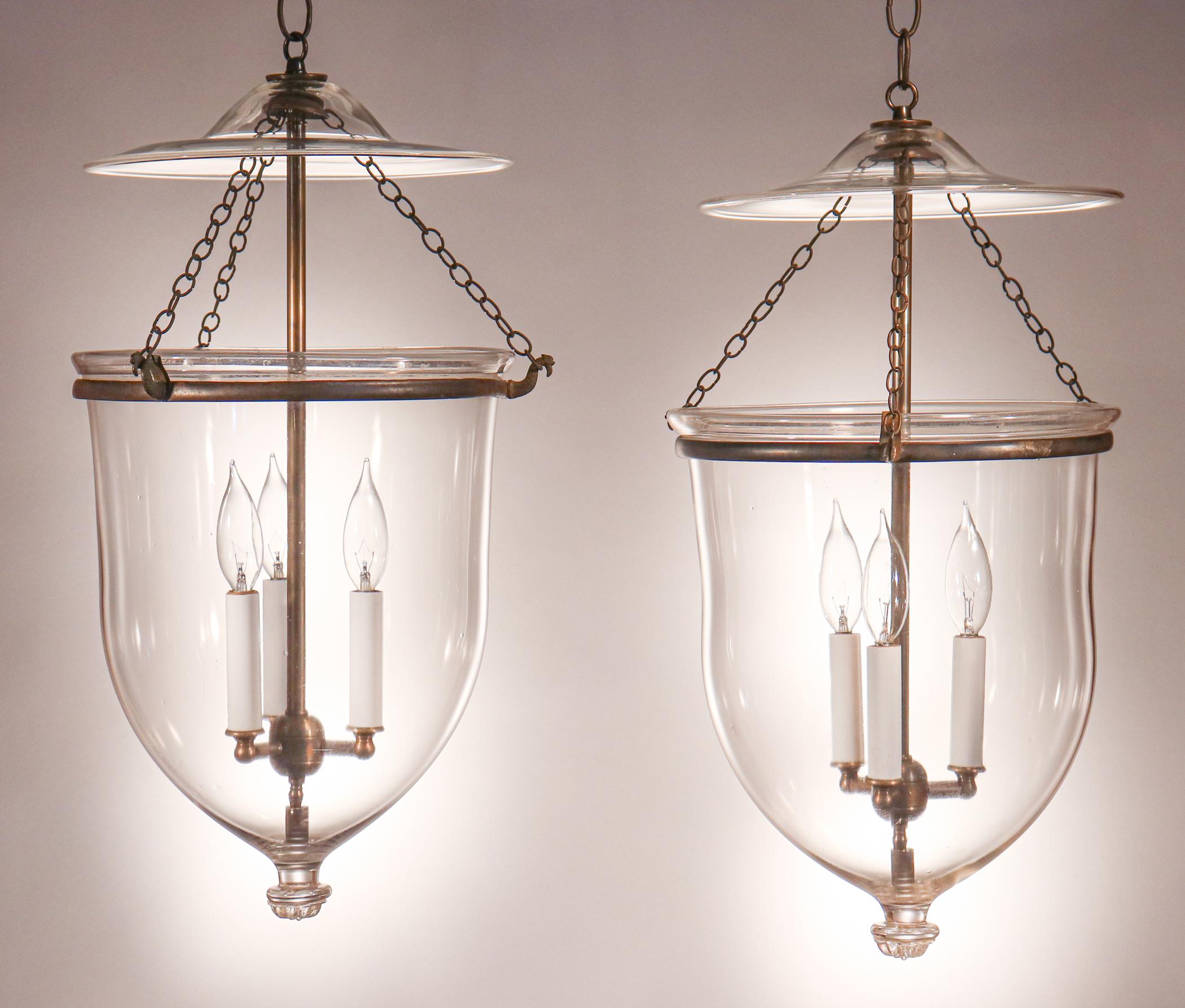 A beautiful pair of hand blown glass bell jar lanterns with original brass bands and chains. These circa 1870 larger-sized English pendants are finished with a distinctive floral design on the brass pontil (see close-up image). The lanterns have