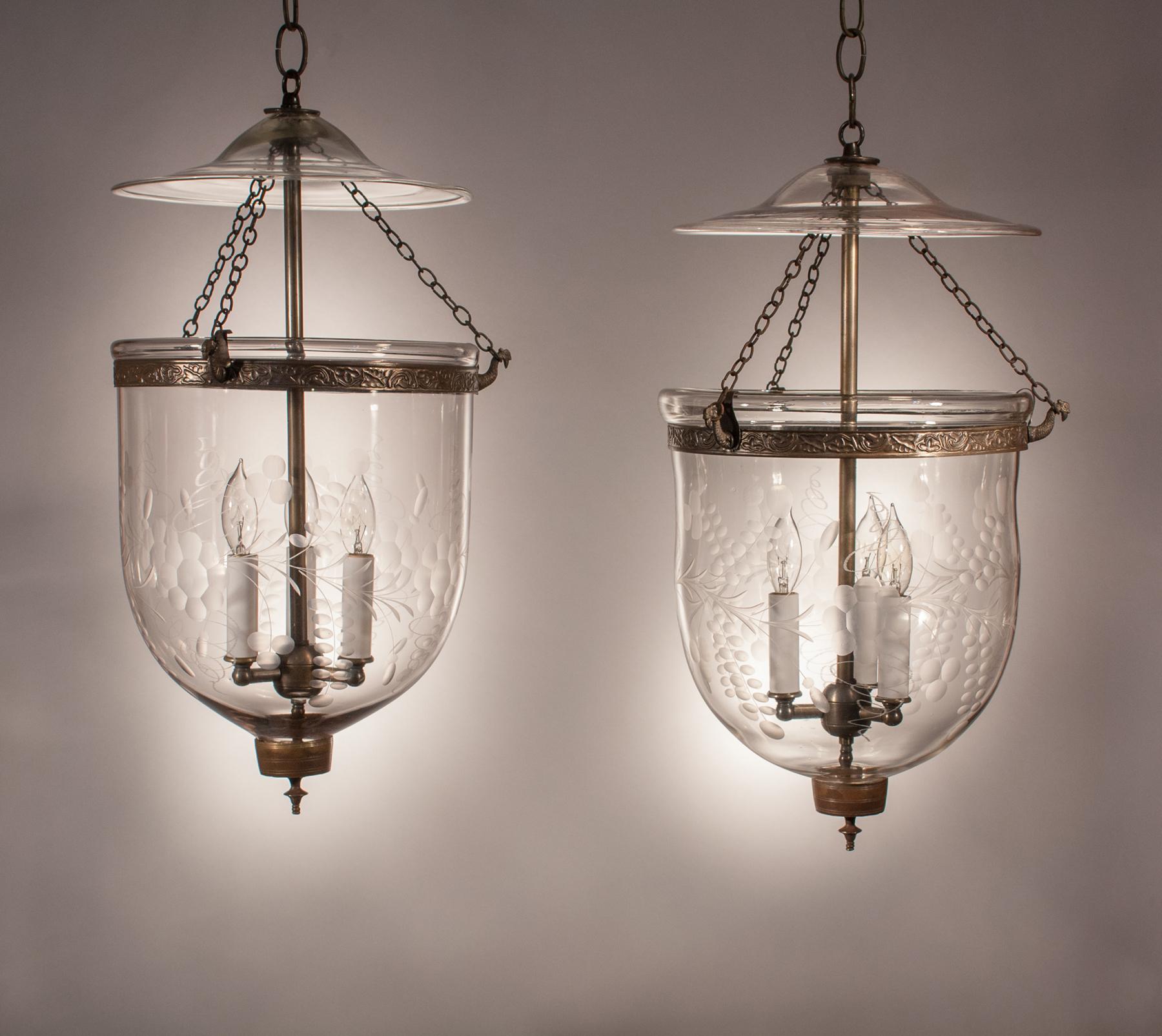 A beautiful pair of English bell jar lanterns, circa 1860, with full form and an etched floral motif. The quality of these antique pendants is excellent, with several desirable air bubbles in the hand blown glass. The brass bands, which have an