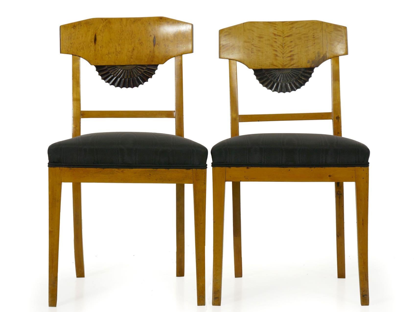 An incredibly attractive pair of Biedermeier style side chairs, they are crafted of birch with finely veneered crest rails of the same over fan-carved ebony stained embellishments in the splat. Probably from the last quarter of the 19th century, the