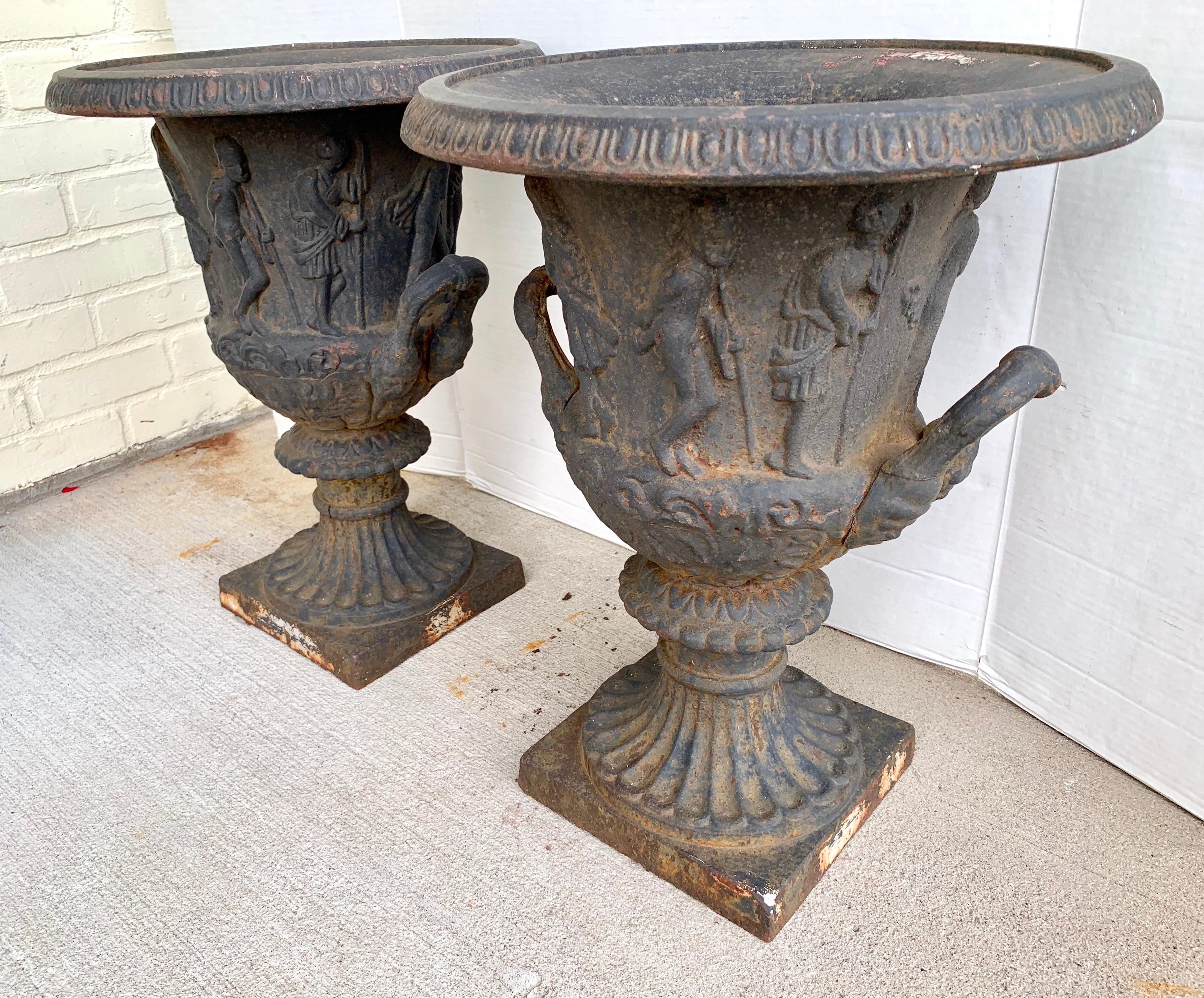 Pair of 19th century neoclassical heavy cast iron urns with an embossed Greco Roman figural motif all around.