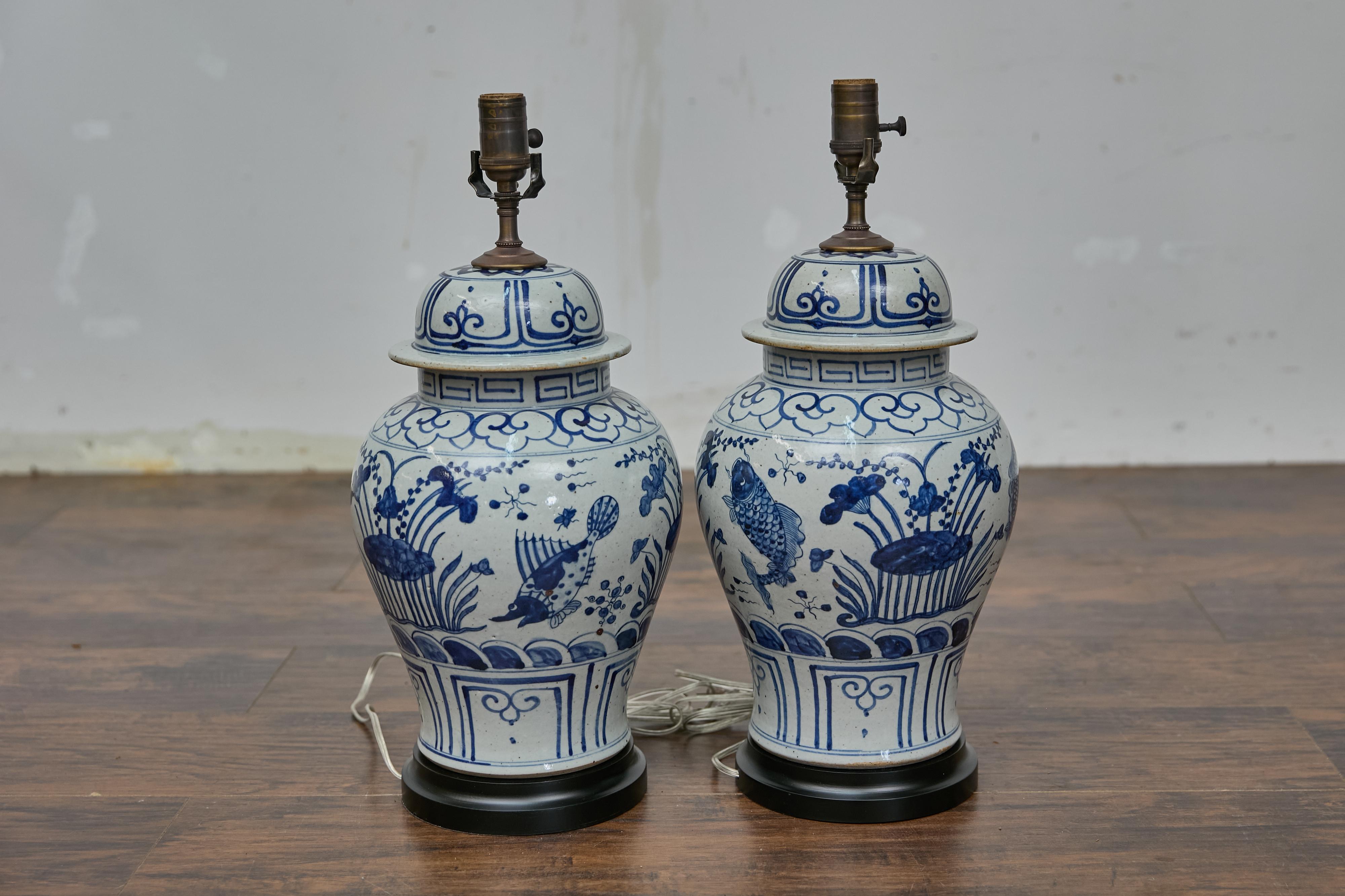 Paire de lampes de table en forme de jarres en porcelaine blanche et bleue avec des motifs de poissons et de plantes aquatiques de bon augure, câblées pour les États-Unis. Transformez votre espace avec cette élégante paire de lampes de table