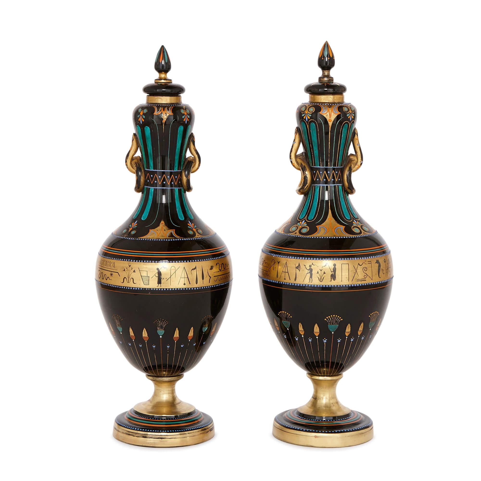 These unusual and striking Bohemian glass vases take ovoid shape, and are made from opaque black glass, called hyalithe. They are decorated in the Egyptian style. To the centre of the body of each vase is a gilt band decorated with Egyptian