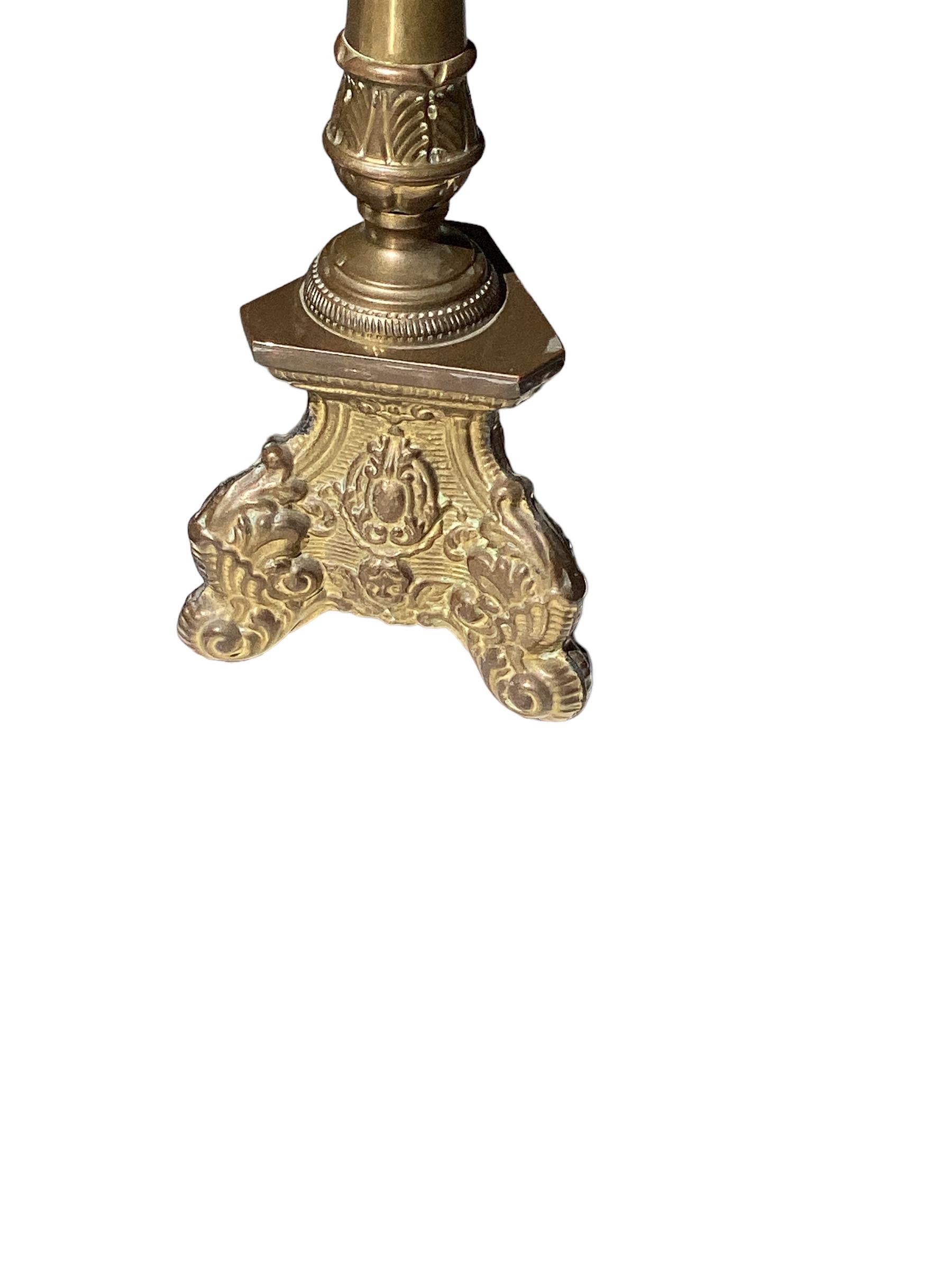 Pair of antique solid brass candlesticks with later conversion to electricity. Each candlesticks sits on a triangular base with repoussé relief decoration. Lamps are newly wired and in good working condition.