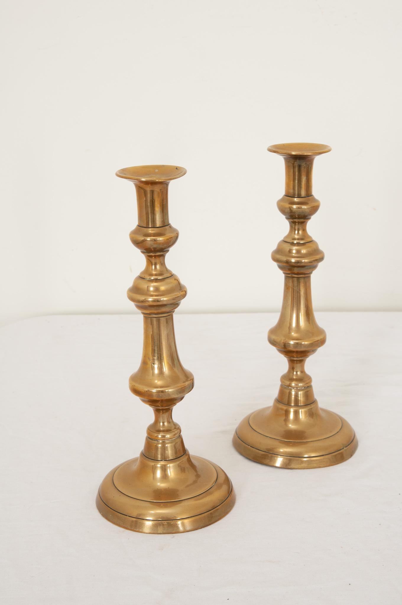 Pair of antique solid brass candlesticks. Finely crafted turned spindles give this pair a look of beautiful classic style and simplicity. Heavy with a smooth patina this set would be perfect to flank artwork or for table illumination. Be sure to