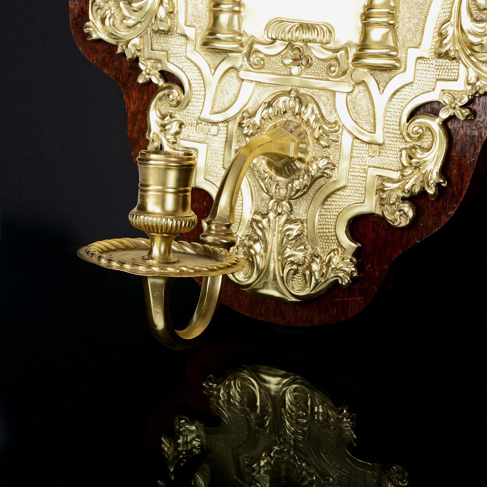 Supported on polished wood mounts, this pair of highly decorative antique Britannia silver-gilt wall sconces are hand-chased in an 18th century style that would have been popular circa 1730. Britannia silver is more pure than sterling silver (958